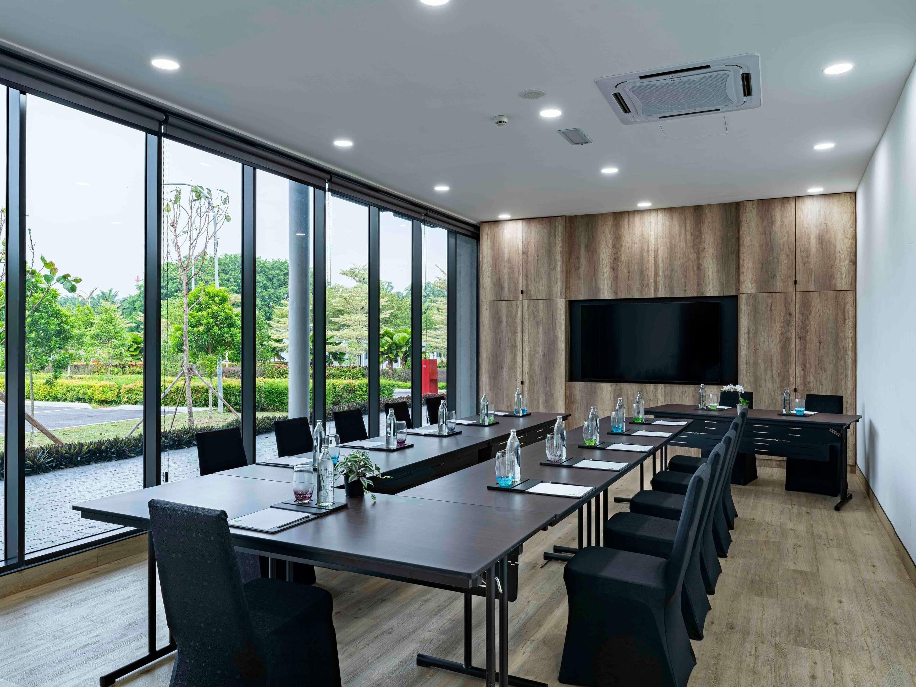 A conference room with a long table, chairs, a TV screen, and large windows.
