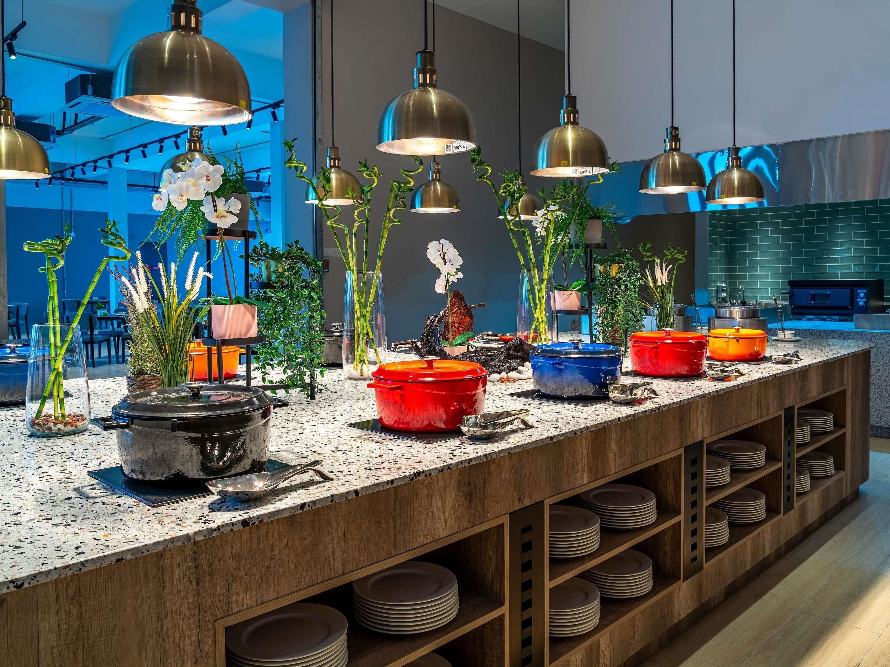 A modern kitchen with a long countertop, multiple pots, and a variety of plants.
