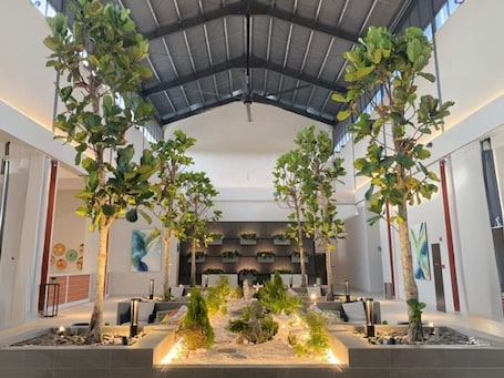 A modern indoor space with a high ceiling, large windows, and a central seating area with planters.