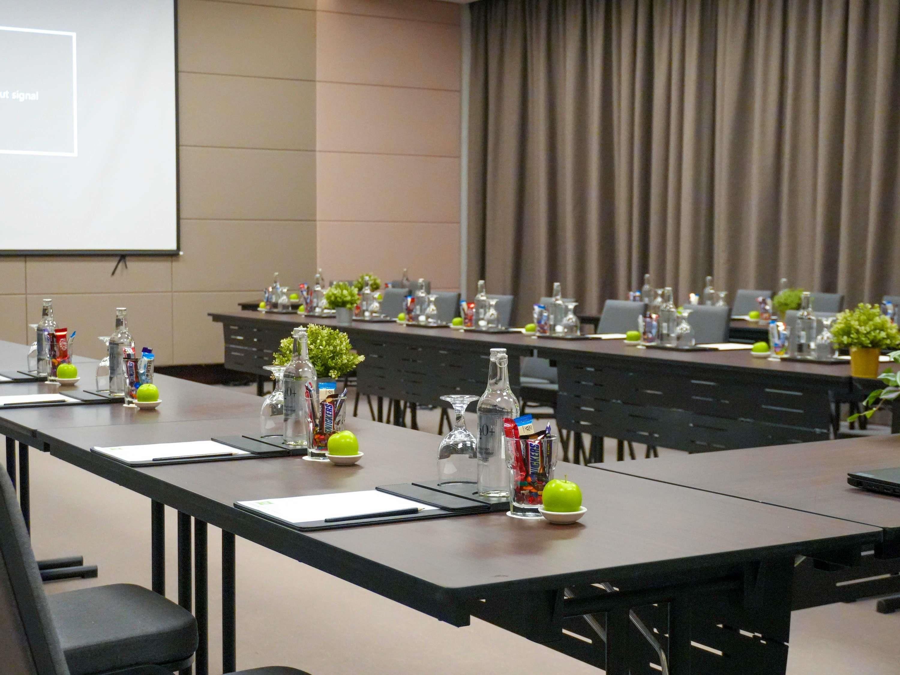 Ein Konferenzraum mit langen Tischen, Stühlen und einer Projektionsleinwand.