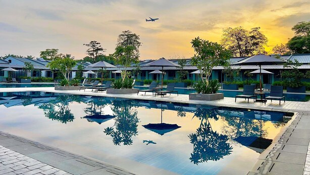 A pool area with lounge chairs and umbrellas, surrounded by buildings with a modern architectural style. - Ibis Styles Sepang Klia (Sepang)