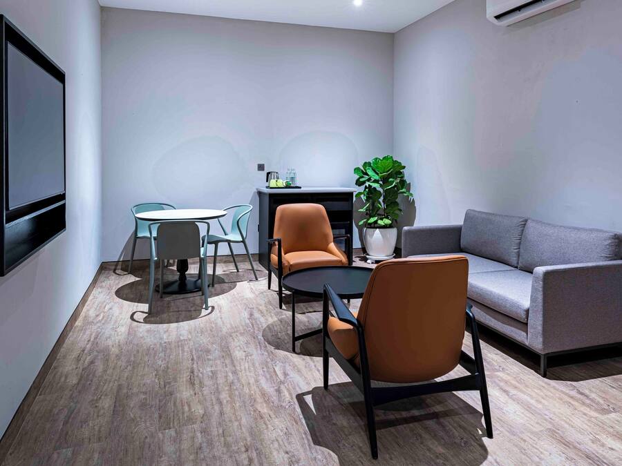 A modern living room with a grey sofa, two orange chairs, a round table, and a potted plant.