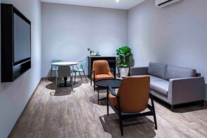 A modern living room with a grey sofa, two orange chairs, a round table, and a potted plant.
