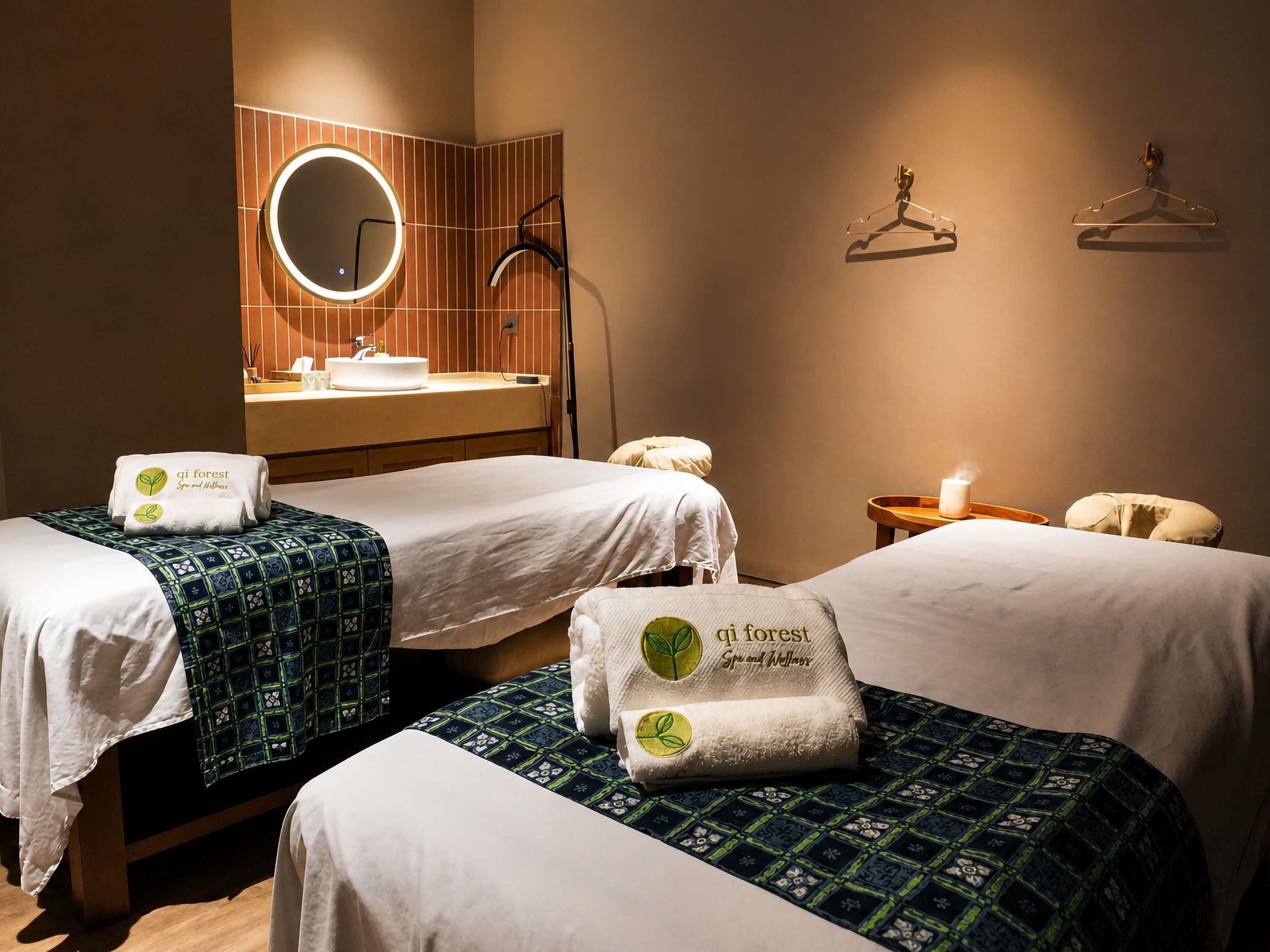 A hotel room with two beds, a bathroom with a mirror and sink, and a bedside table with a candle.