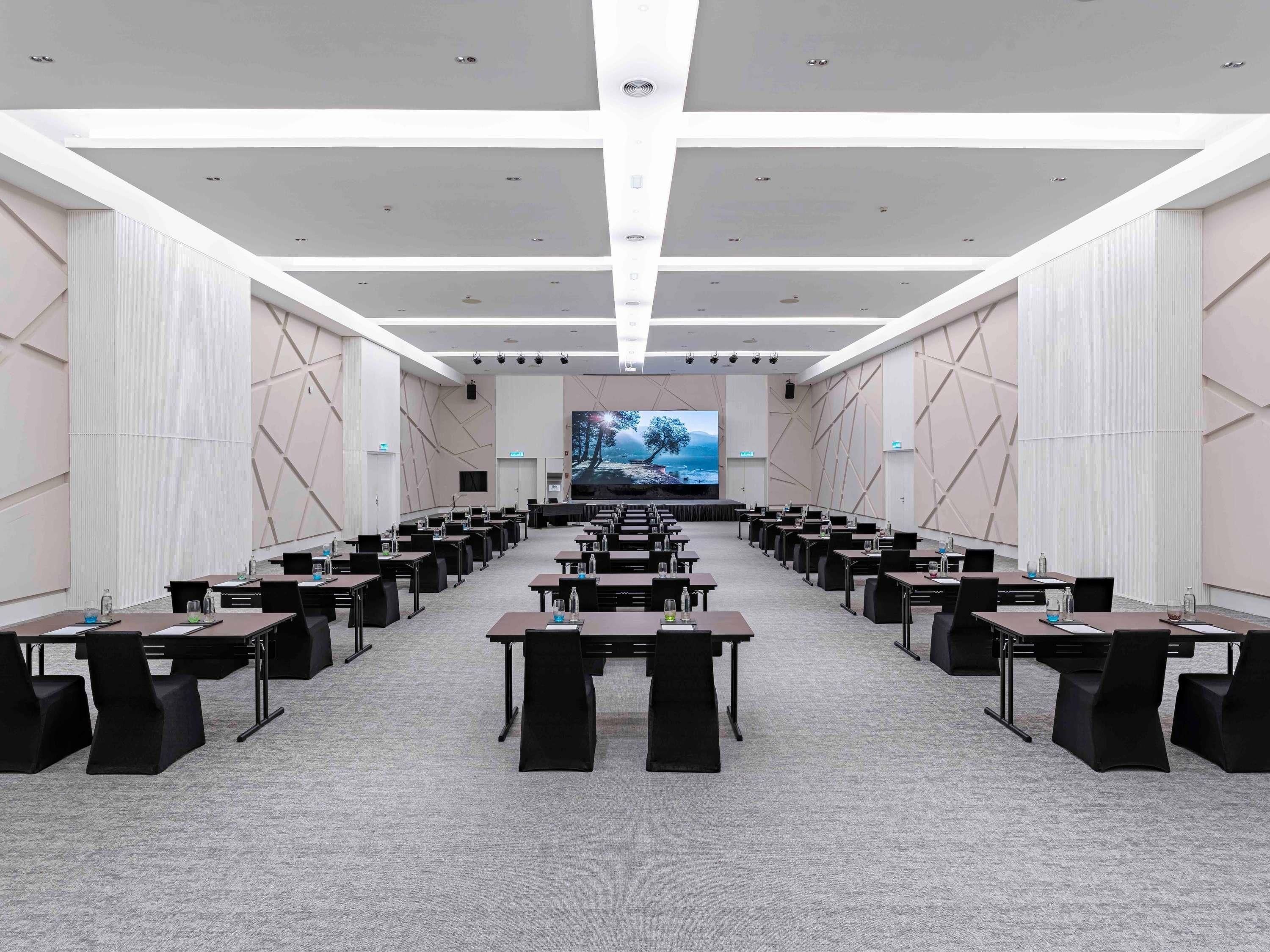 A conference room with a long table, chairs, and a large screen at the front.