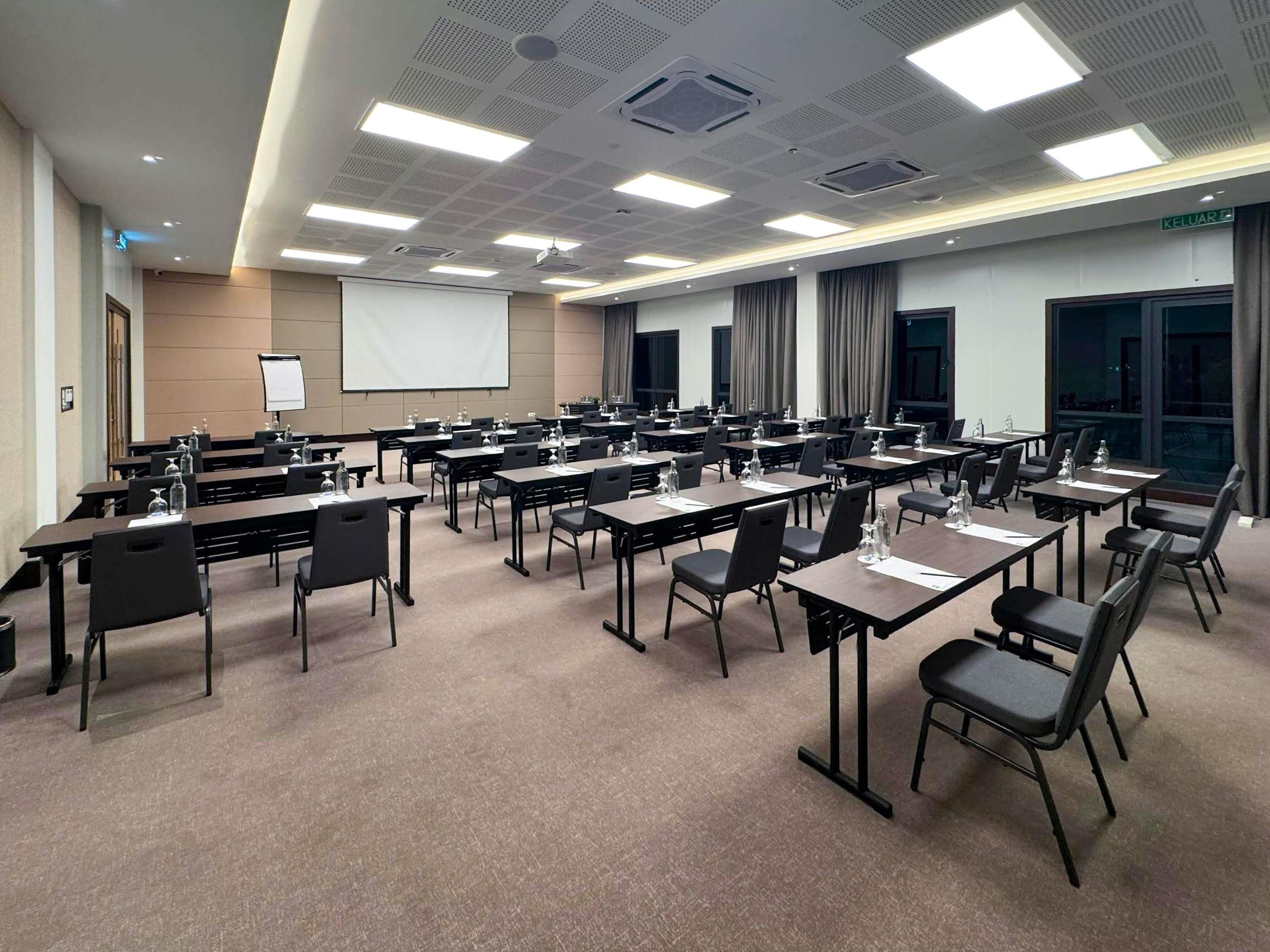 A conference room with multiple tables and chairs, a projector screen, and a large window with curtains.