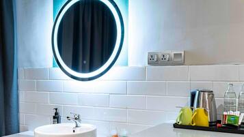 A bathroom with a white sink, a round mirror with a light, and a towel rack with yellow and green towels.