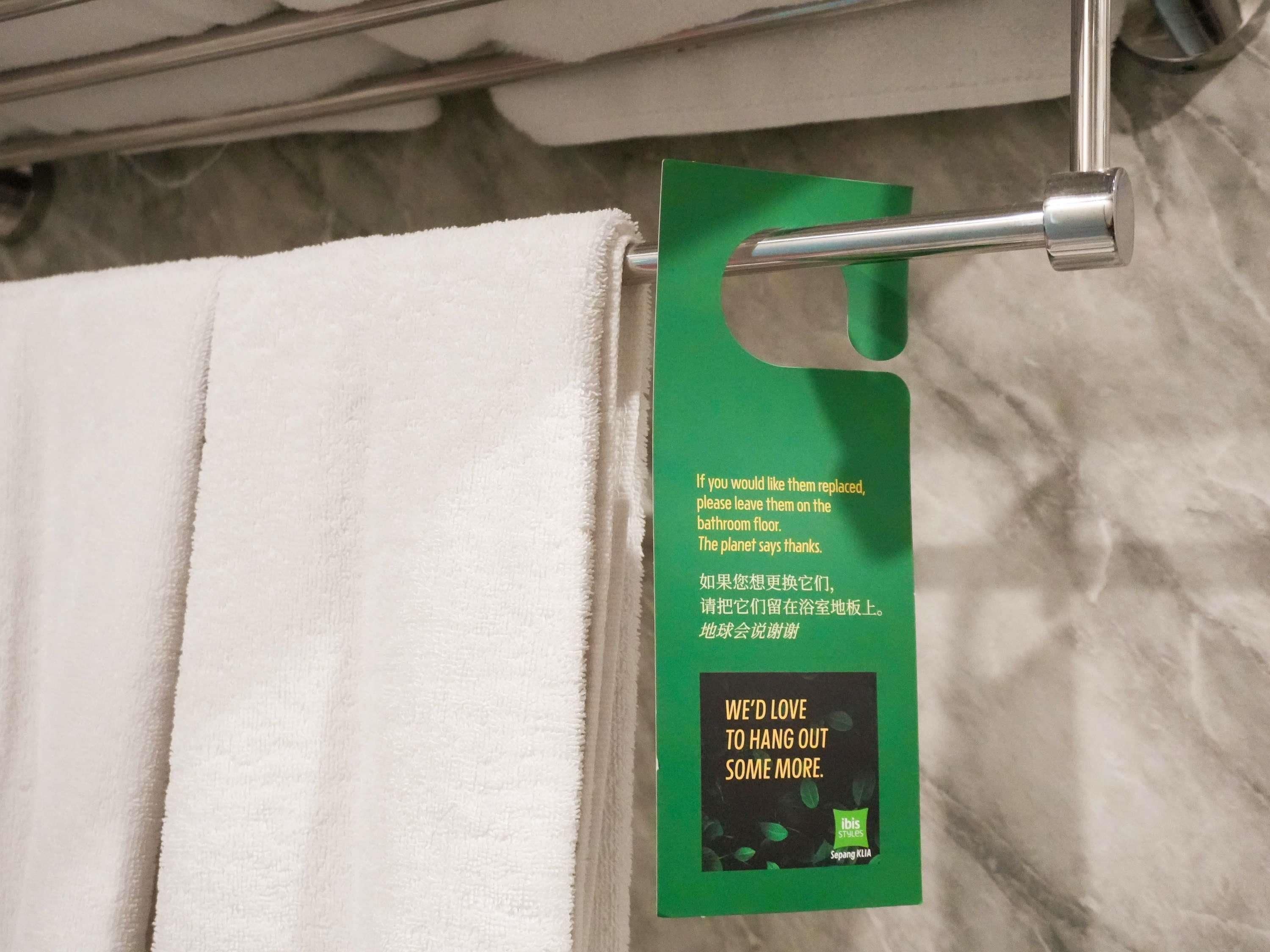 A bathroom towel hanging on a rack with a green tag attached to it.