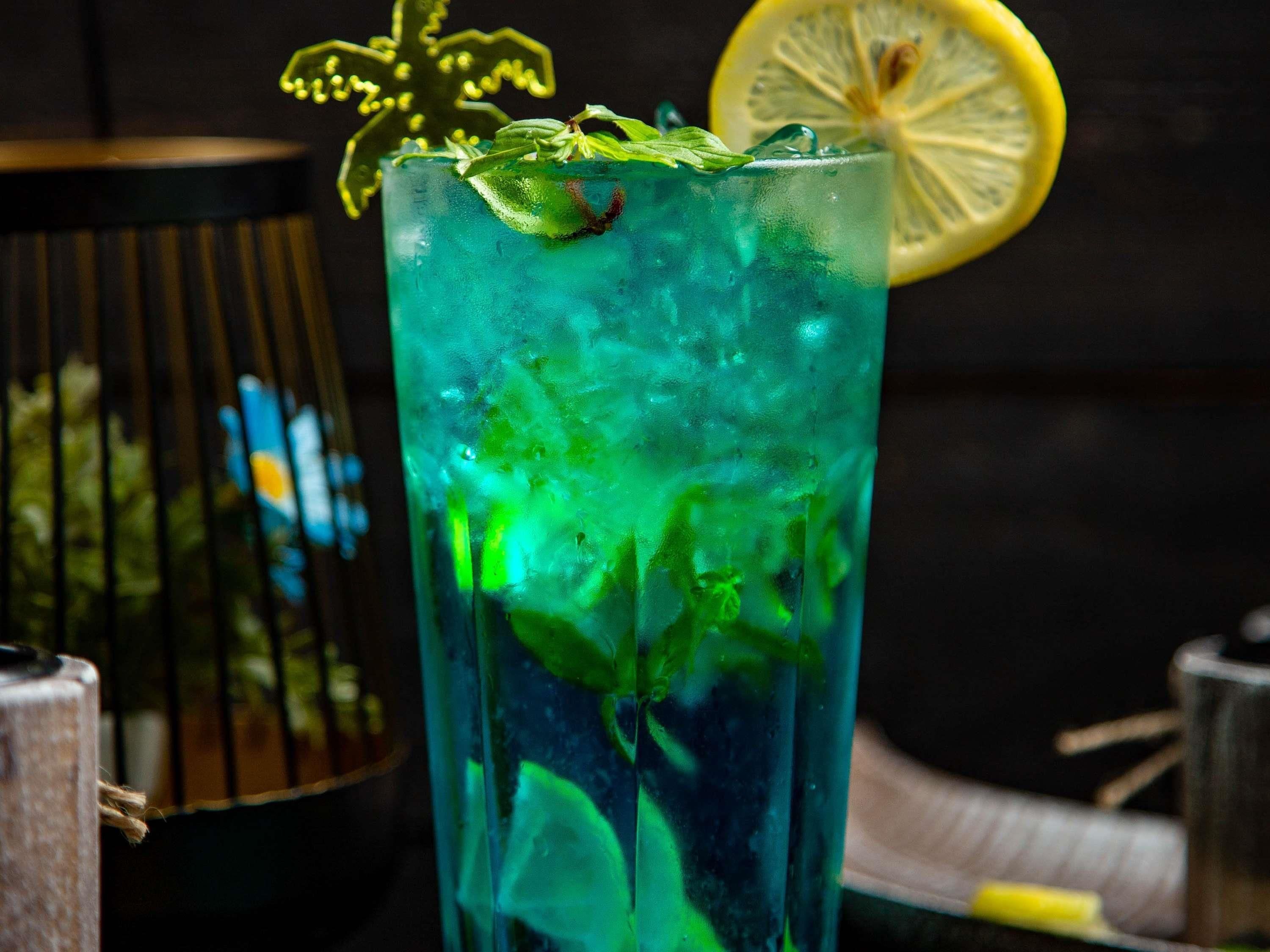 Un vaso alto con una bebida verde, adornado con una rodaja de limón y hojas de menta.
