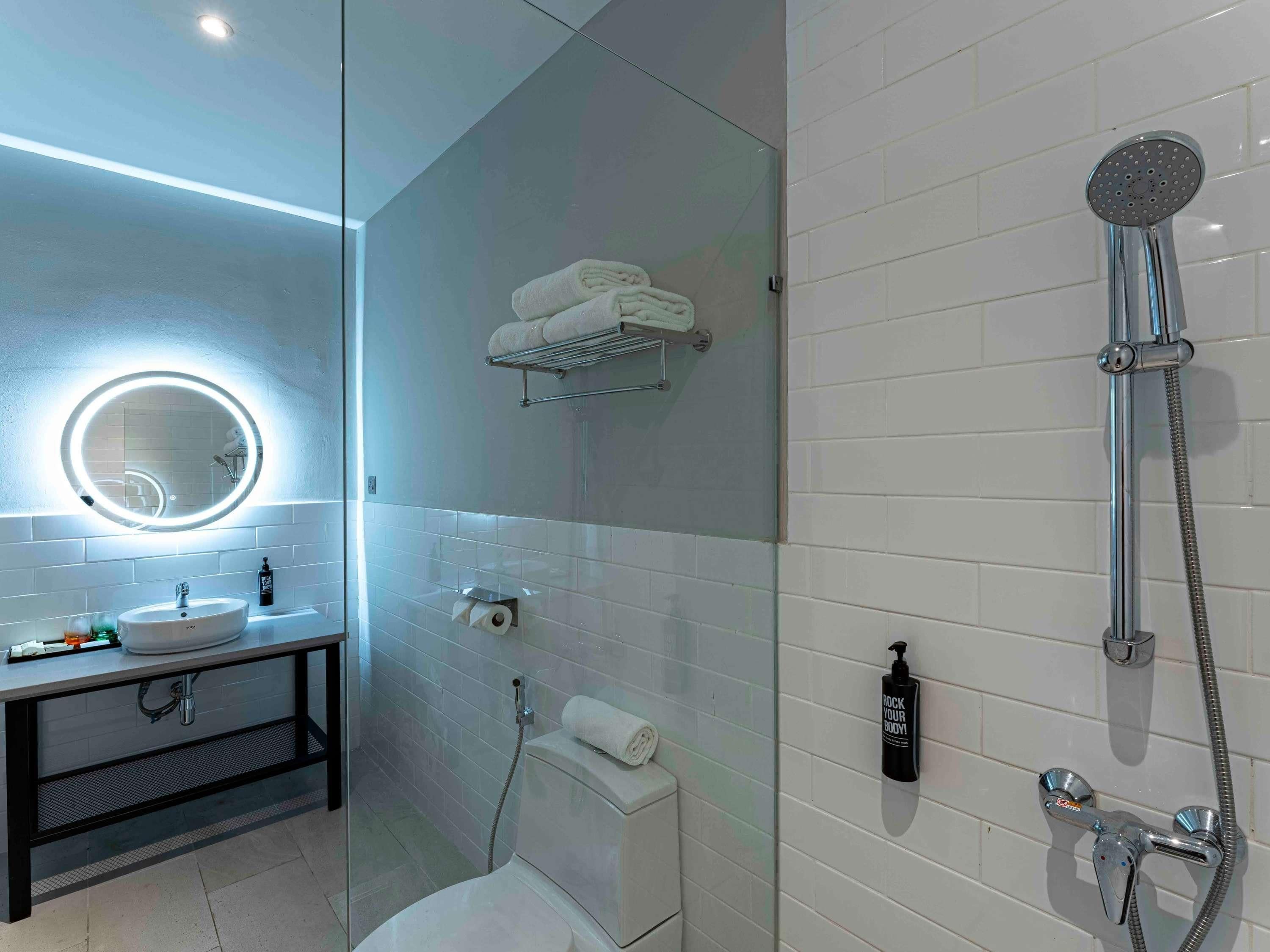 Um banheiro moderno com box de vidro, um espelho redondo com iluminação embutida, pia branca e vaso sanitário.