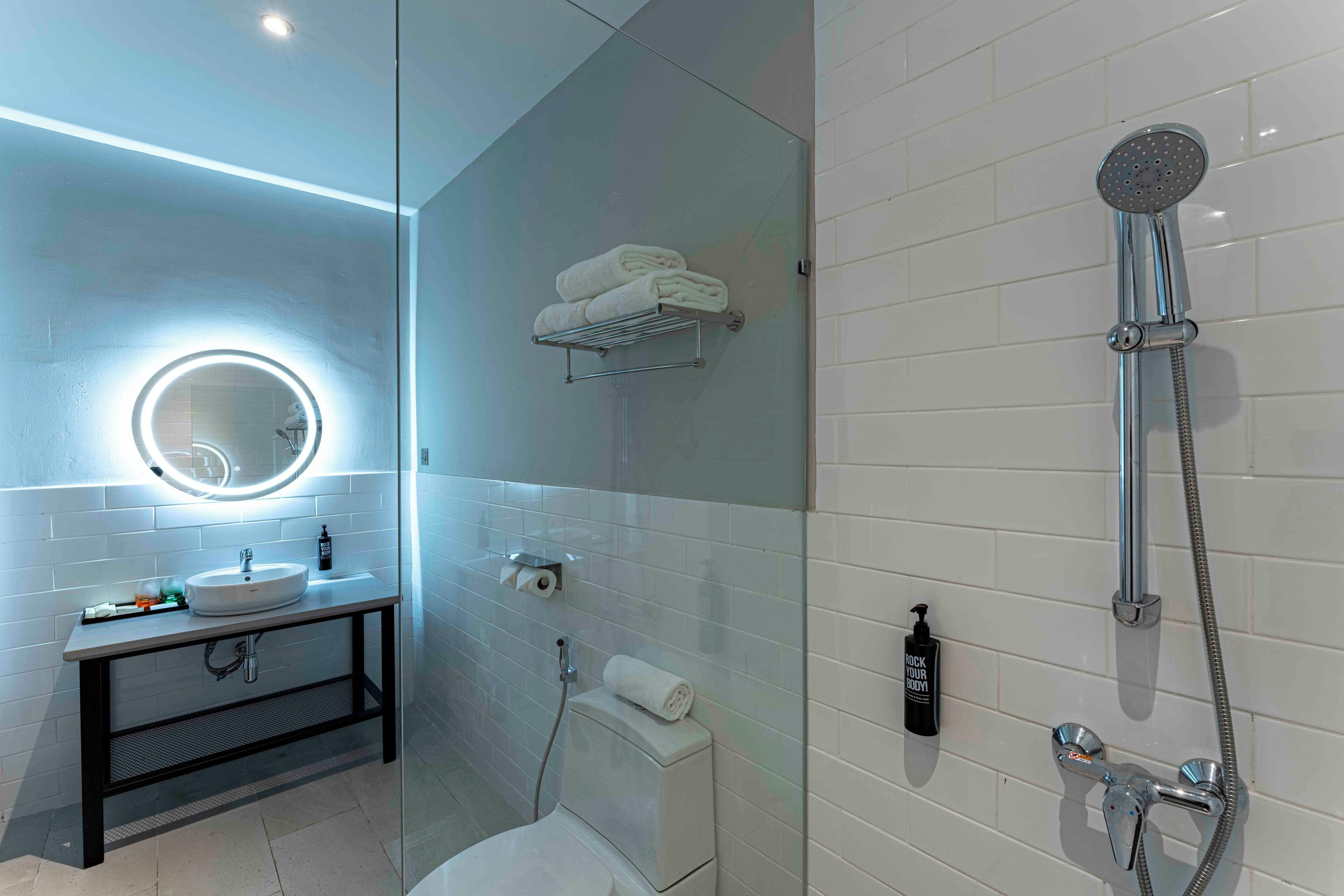 Een moderne badkamer met een douche met glazen wand, een ronde spiegel, een wastafel en een toilet.
