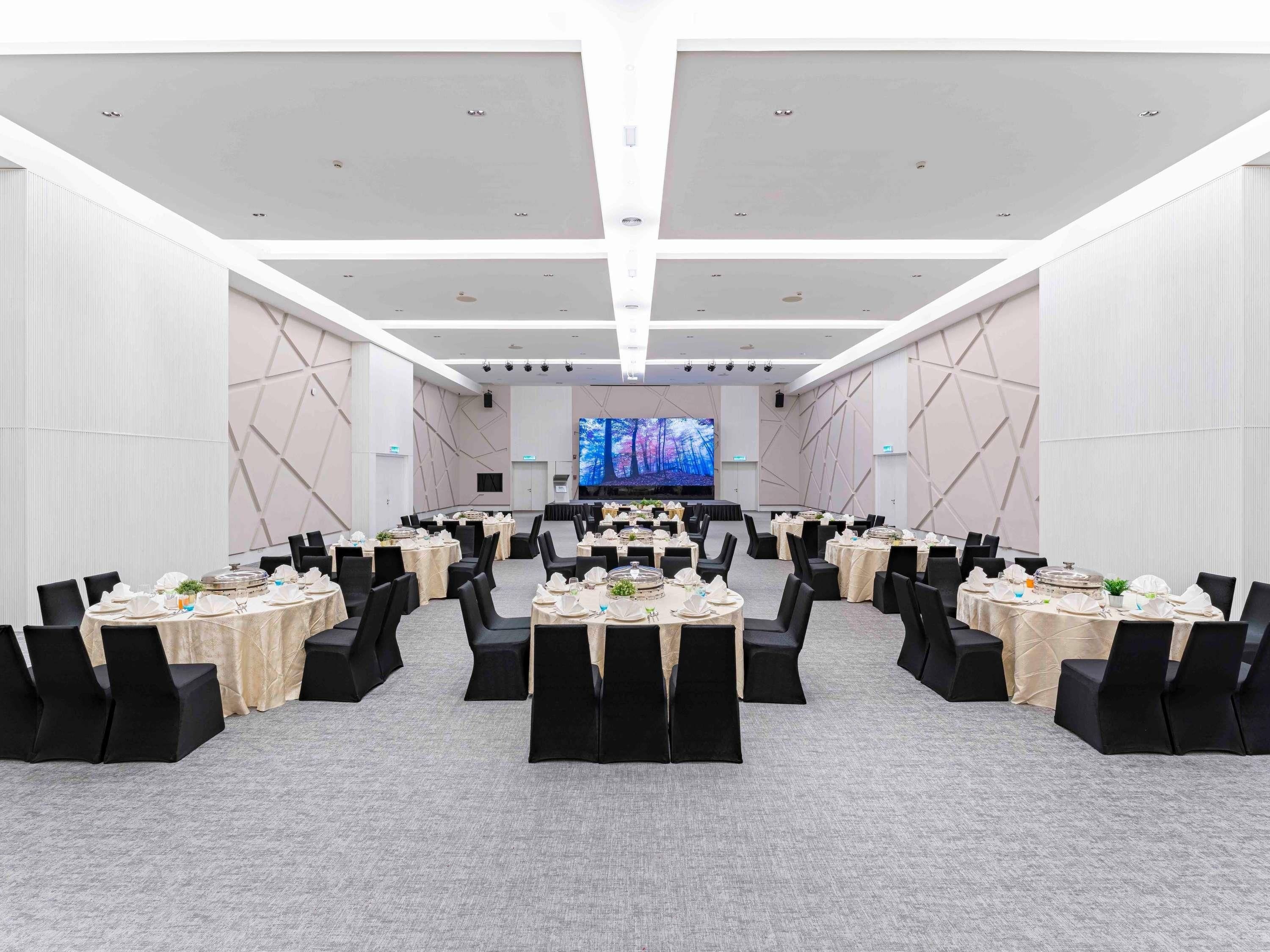 A conference room with round tables, black chairs, and a large screen at the front.