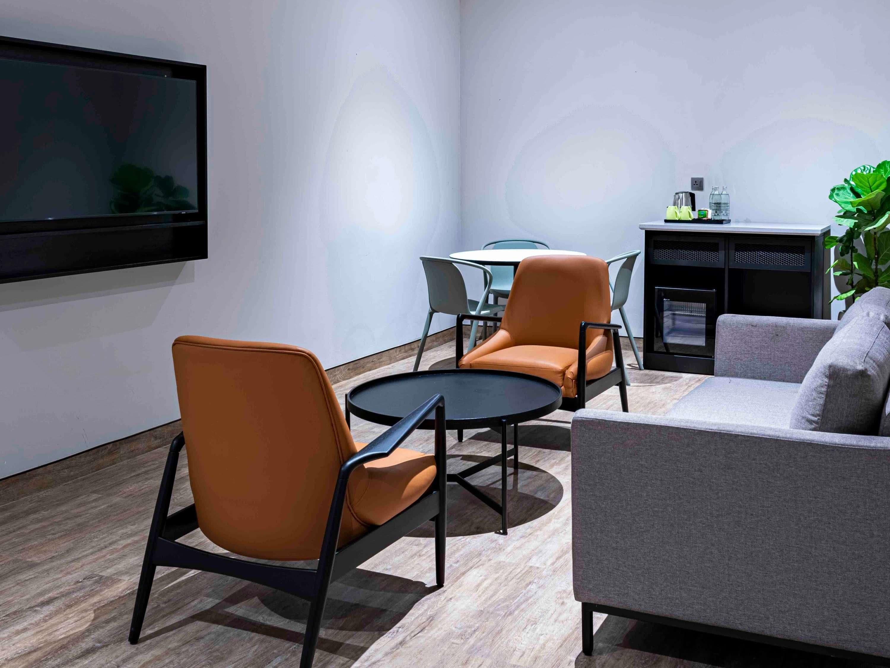 A modern living room with a sofa, two armchairs, a coffee table, and a flat-screen TV mounted on the wall.