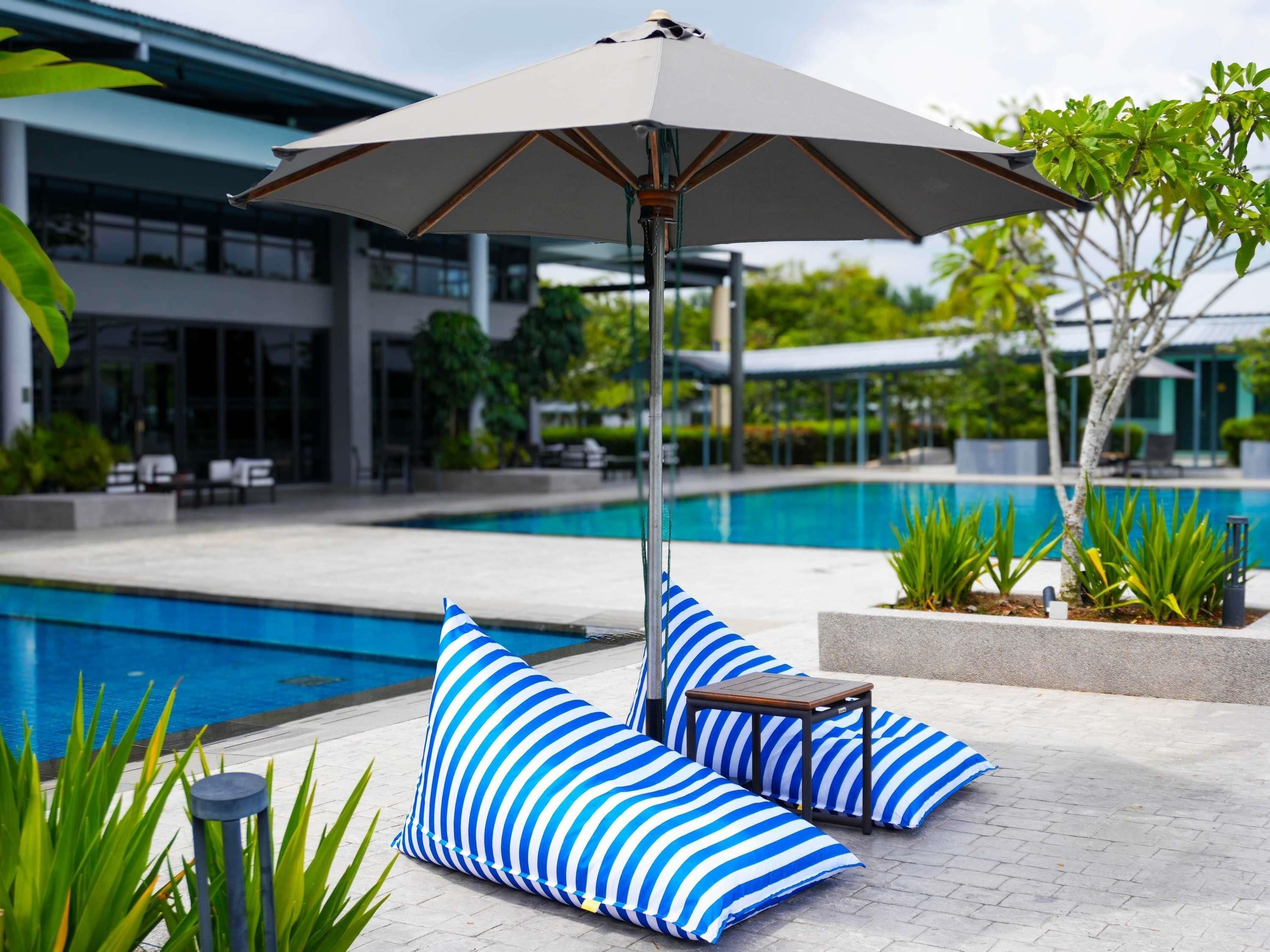 A poolside area with a lounge chair, striped cushions, and a table under a large umbrella.