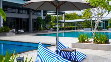 A poolside area with a lounge chair, striped cushions, and a table under a large umbrella.