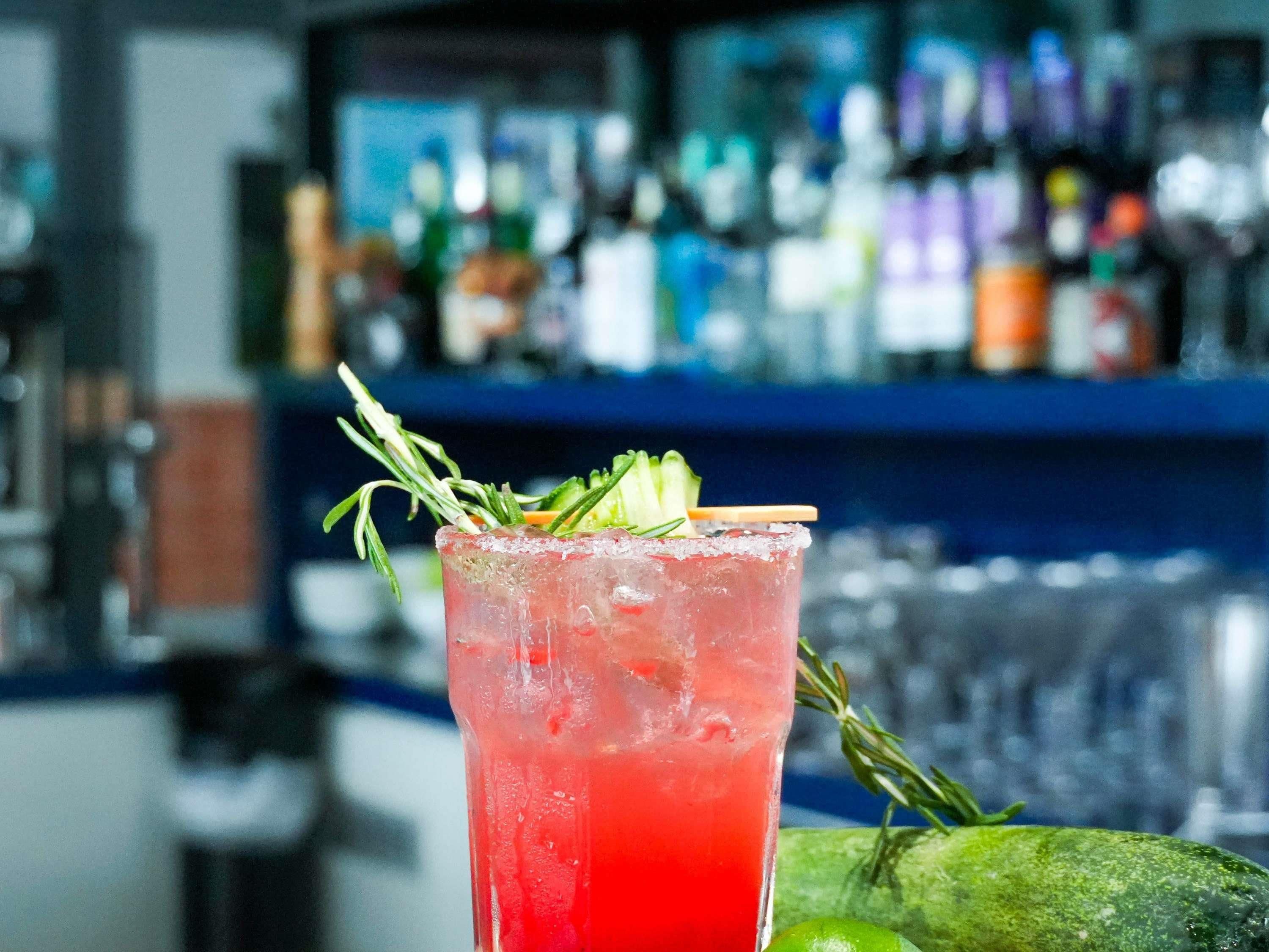A bar setting with a cocktail glass garnished with herbs, a lime, and a cucumber slice.
