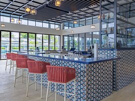 A modern bar area with a glass partition, red bar stools, and a view of the outdoors.