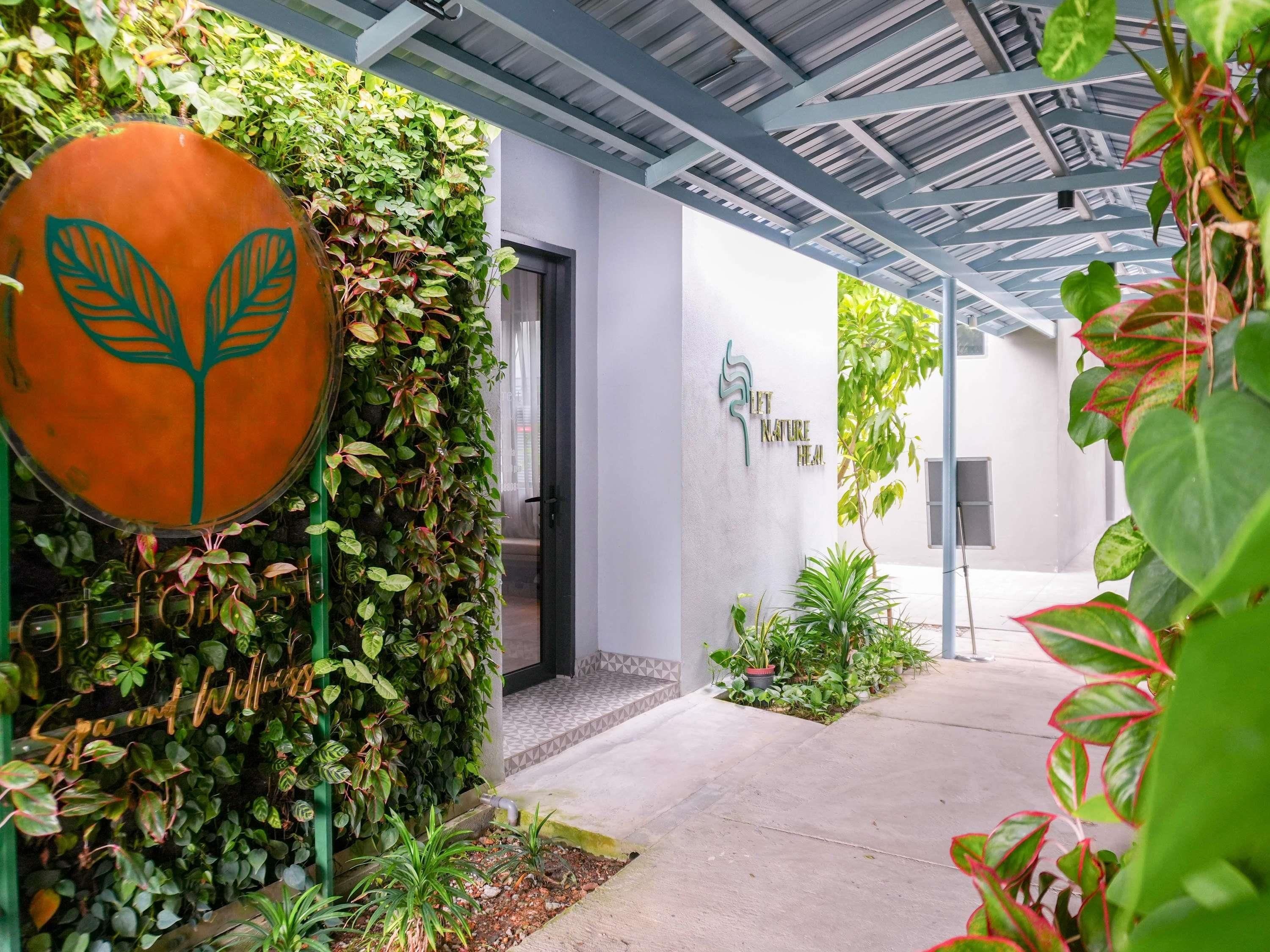 A covered outdoor area with a wall of greenery, a large orange sign with a leaf design, and a sign that reads 'LET NATURE HEAL.'