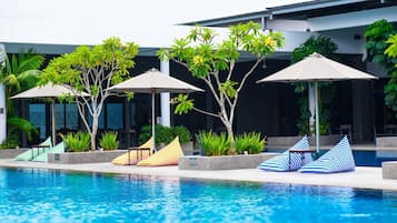 A swimming pool area with lounge chairs and umbrellas, surrounded by greenery and modern architecture.
