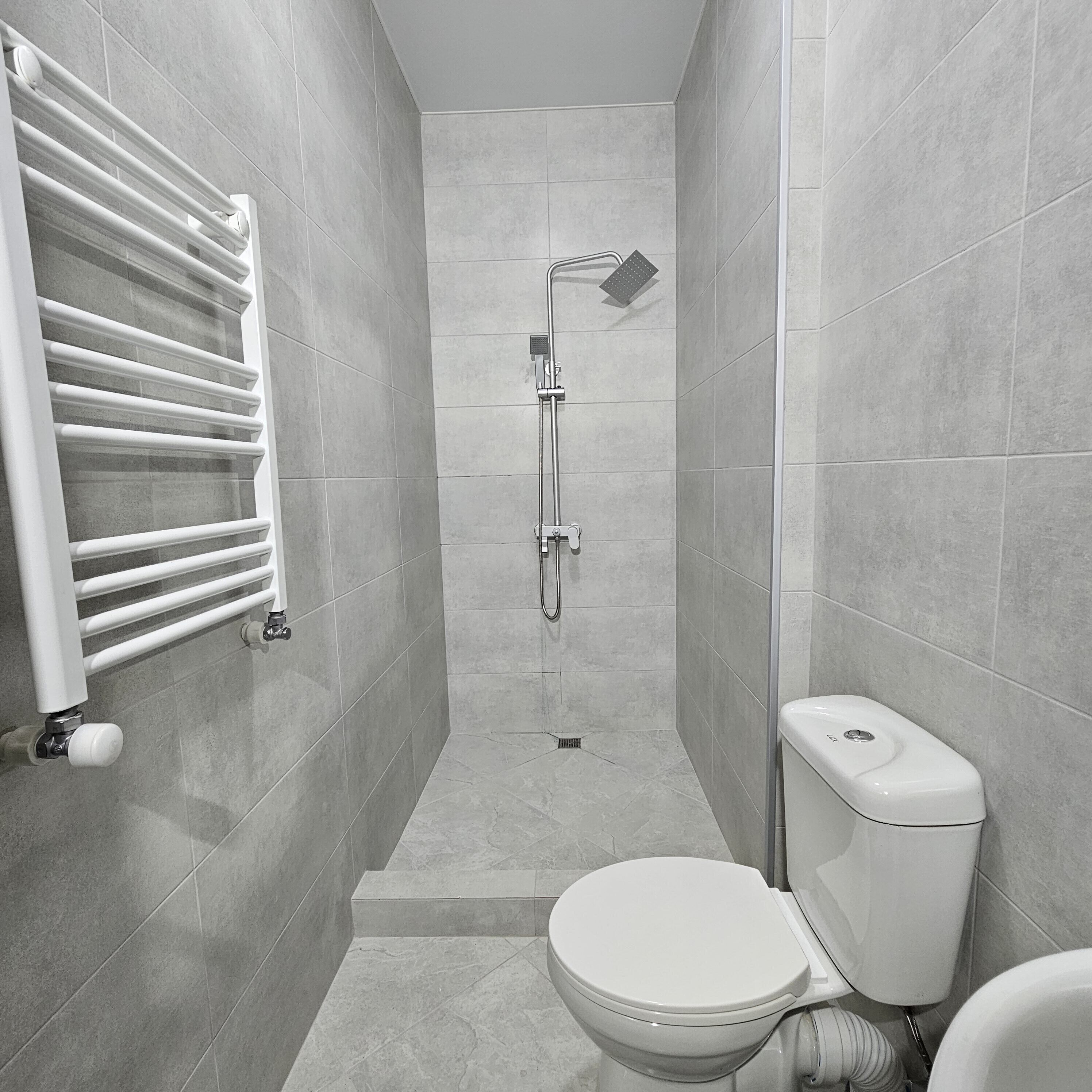 A modern bathroom with a walk-in shower, a toilet, and a towel rack.