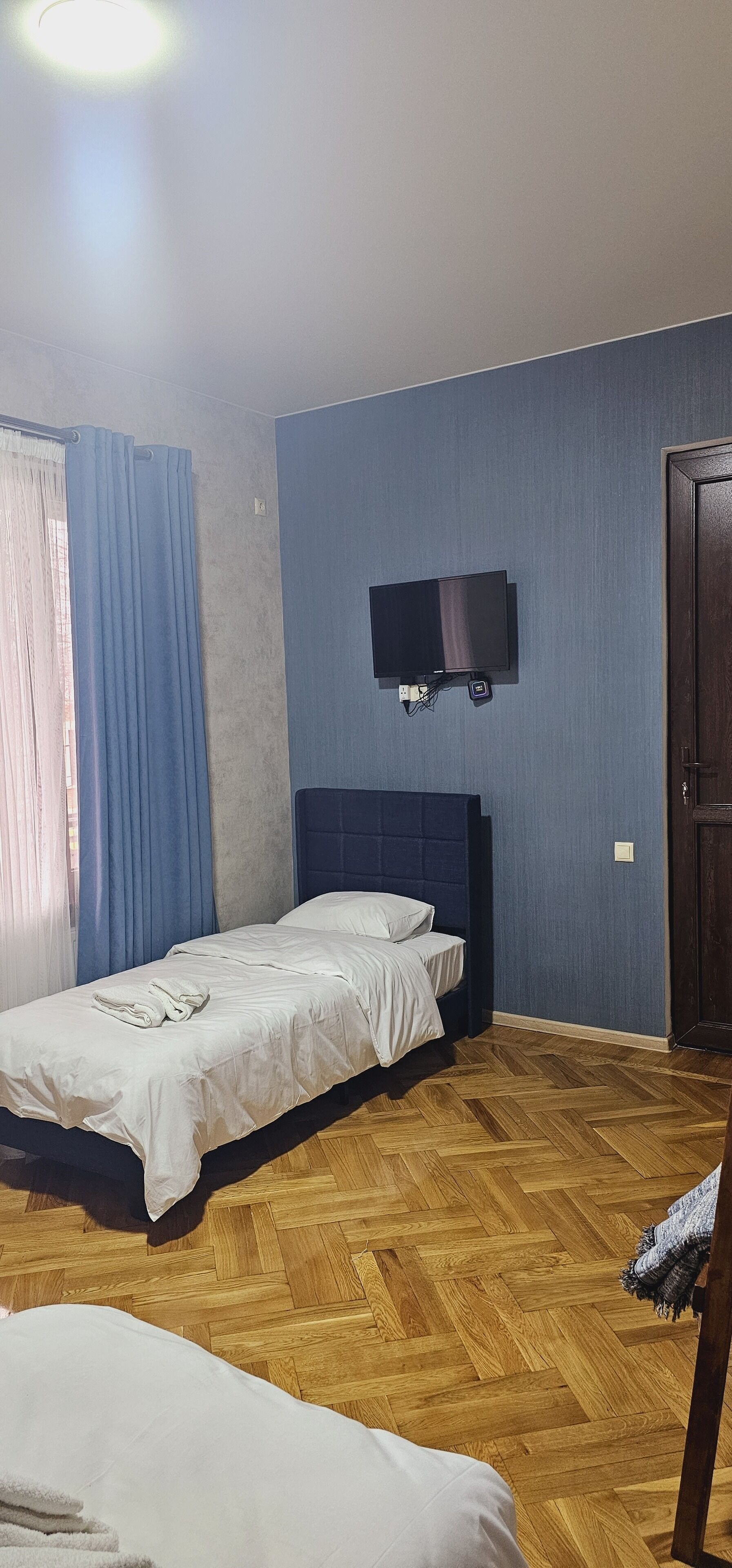 A bedroom with a bed, a television mounted on the wall, and a wooden floor.
