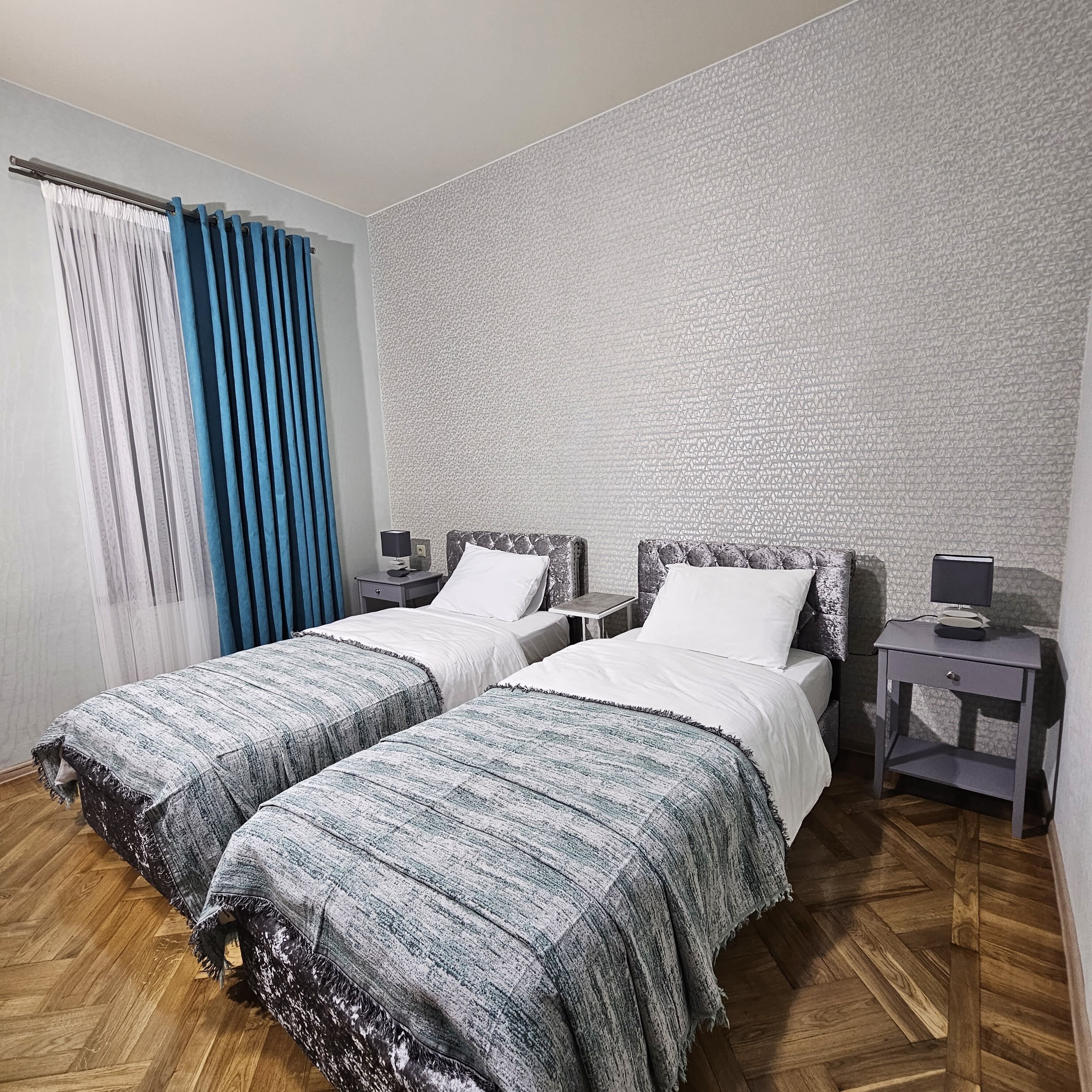 A double bed room with two bedside tables, a nightstand, and a patterned wall.