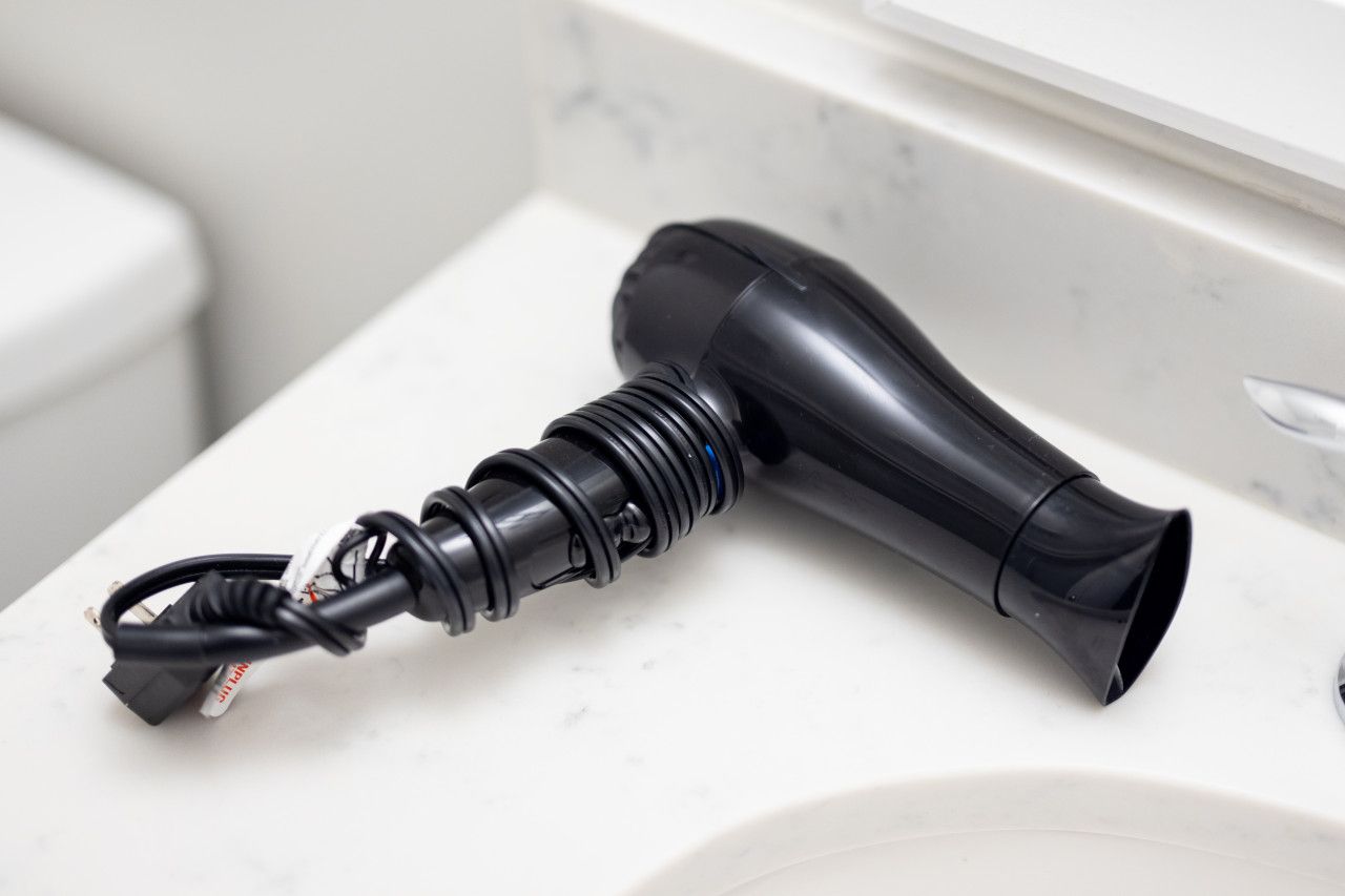 A black hairdryer on a white bathroom countertop.