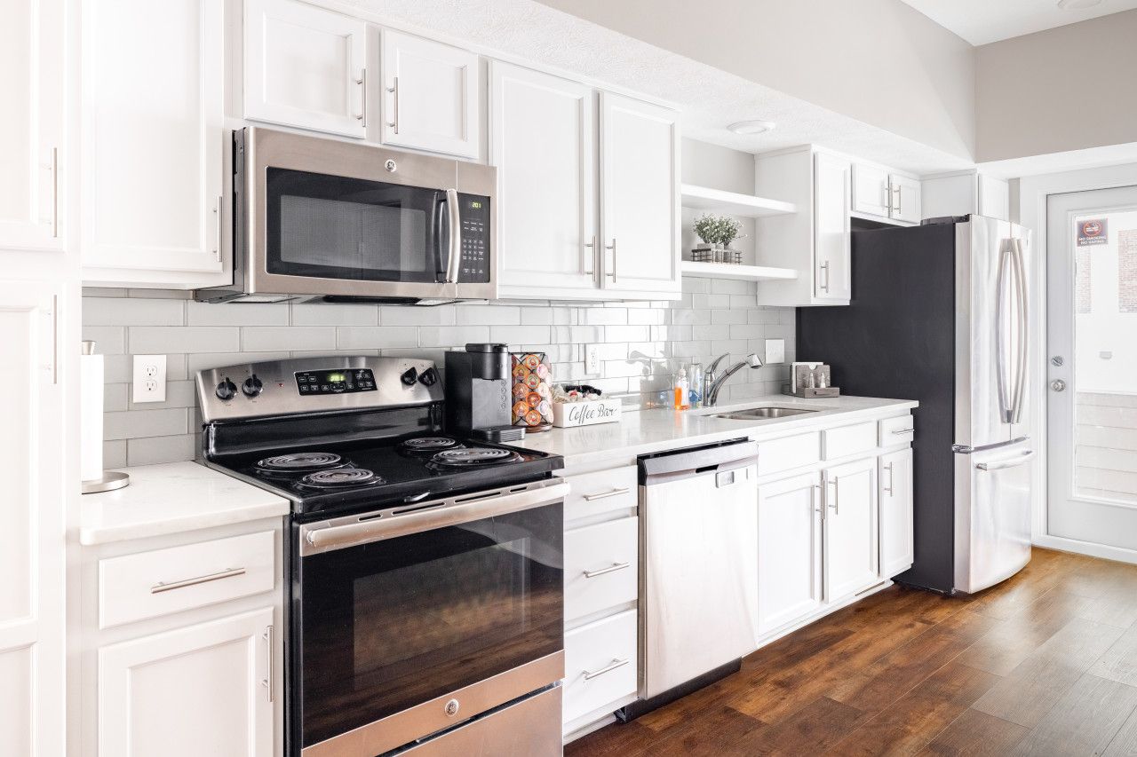 A modern kitchen with white cabinetry, stainless steel appliances, and a black refrigerator.