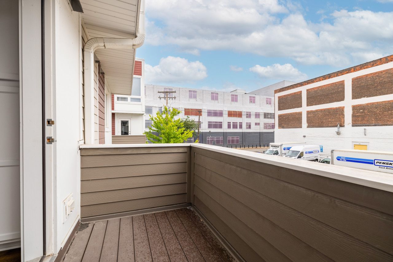 A corner balcony with a view of a parking area and a building with multiple garage doors.