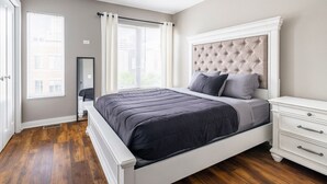 A bedroom with a large bed, a nightstand, a mirror, and a window with curtains. - Luxury Downtown Townhome w/ Private Garage Unit 5 (Cleveland)