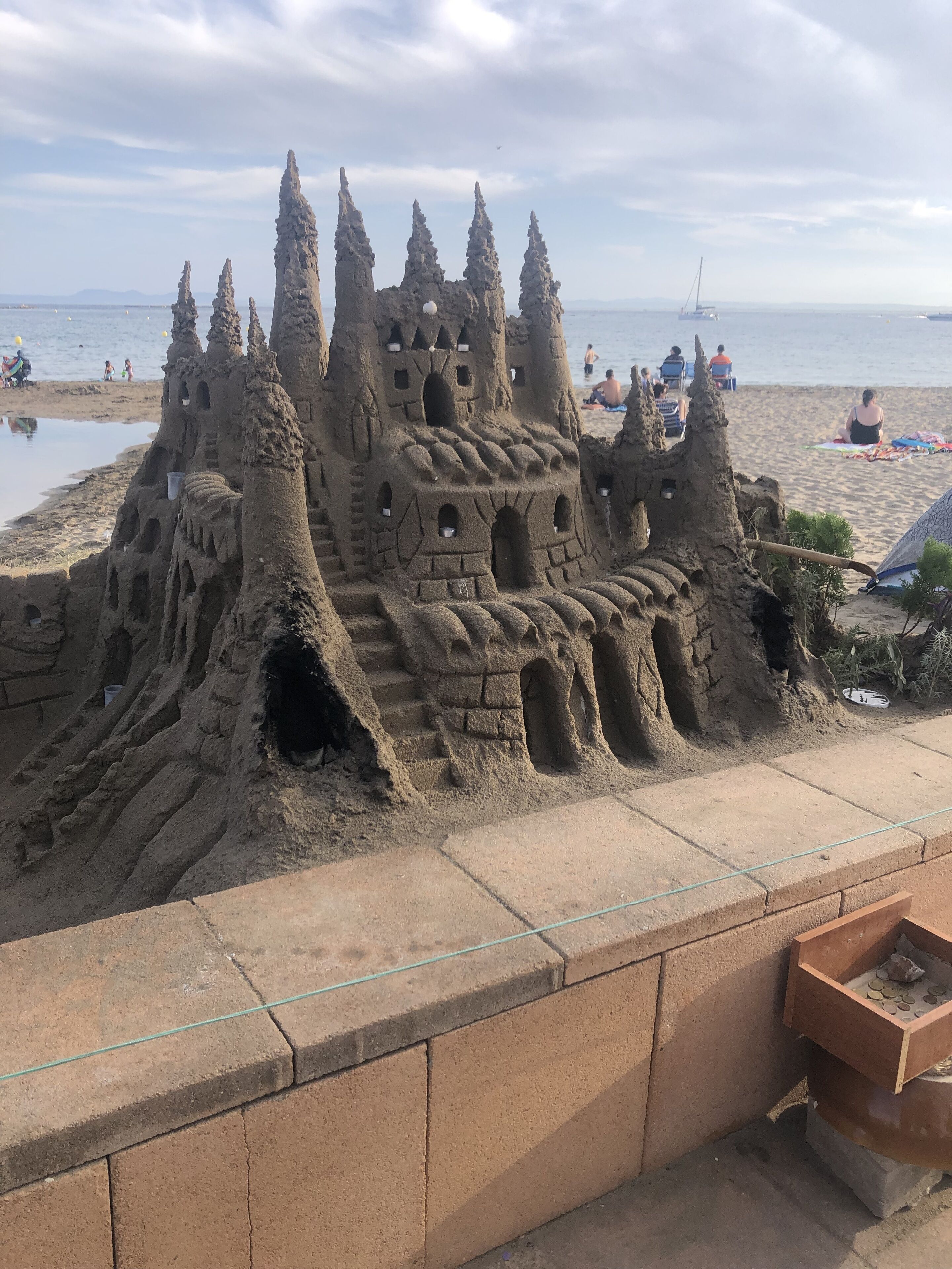 Un grande castello di sabbia con numerose torri e finestre, situato su una spiaggia sotto un cielo sereno.