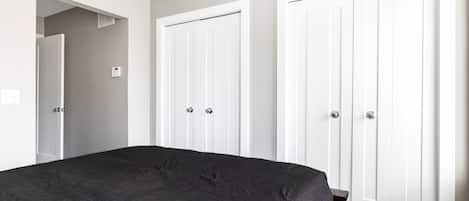 A bedroom with a large bed, two white wardrobes, and a door leading to another room.