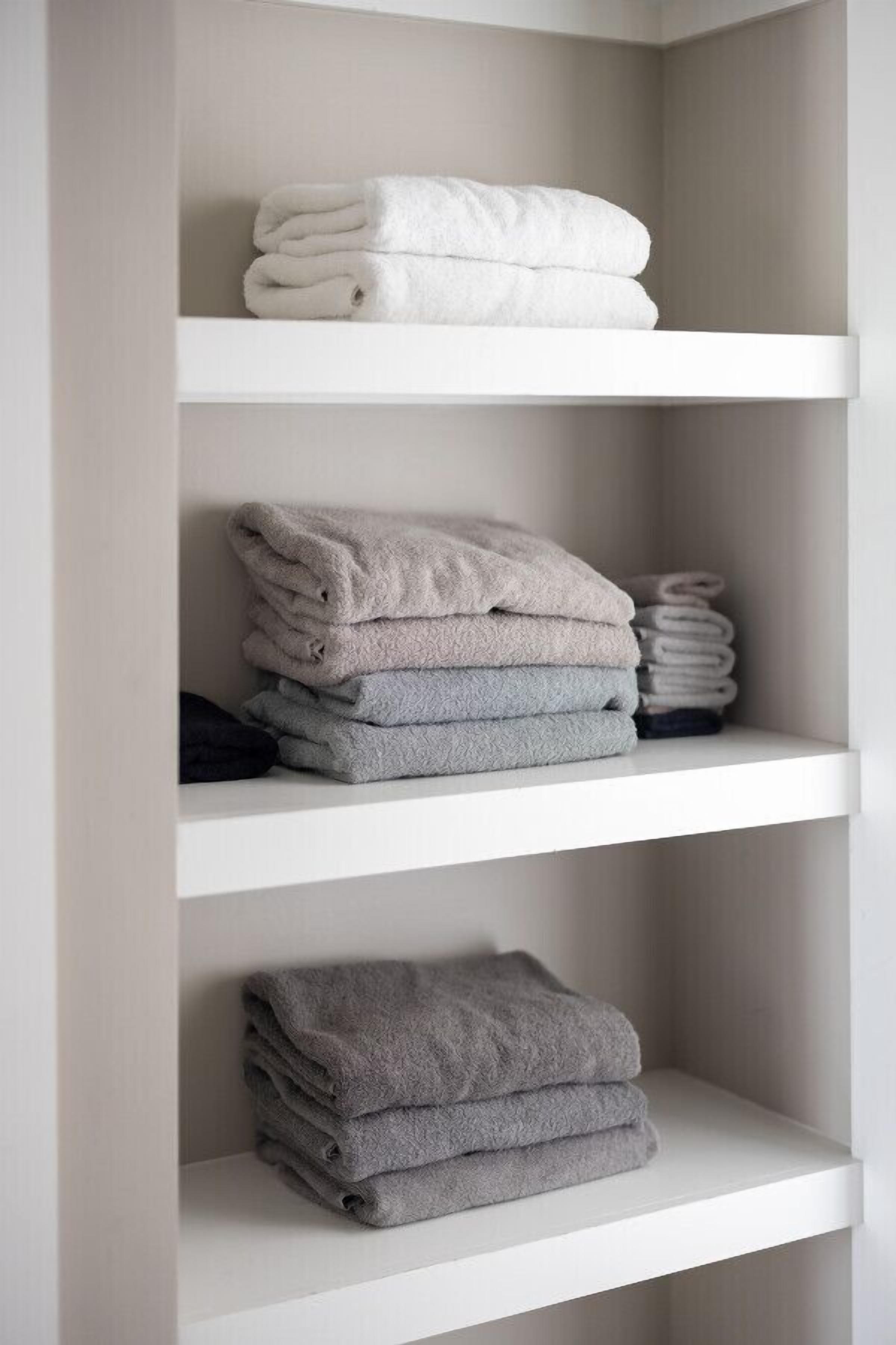 Une étagère blanche où sont pliées avec soin des serviettes de différentes nuances de blanc et de gris.