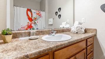 A bathroom with a granite countertop, a white sink, wooden cabinets, a potted plant, a towel rack, and a mirror.