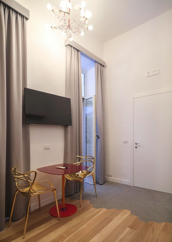 Una habitación moderna con un televisor de pantalla plana en la pared, una mesa redonda con dos sillas, una araña y una puerta con un ventanal.