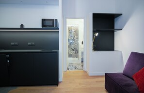 A modern kitchen with a microwave, a built-in oven, and a coffee machine. There is a purple sofa and a small table with a red cushion. - Youroom Margutta (Rome)