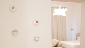 Moderni hotellihuone, jossa on pelkistetty sisustus. Huoneessa on suuri sänky, sohva ja seinä, joka on koristeltu sydämenmuotoisilla koriste-esineillä.