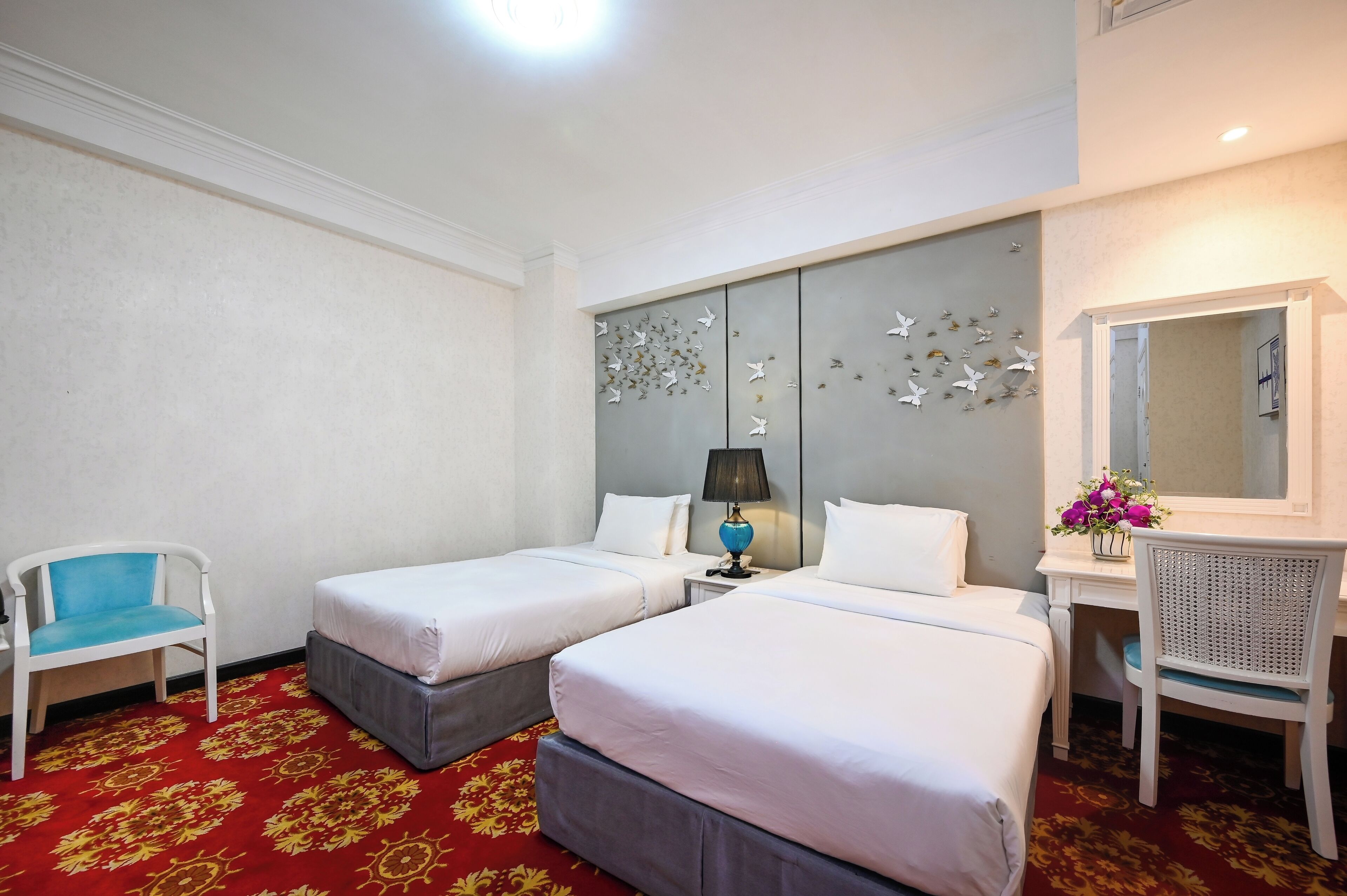 Ein Hotelzimmer mit zwei Betten, einem Schreibtisch, einem Stuhl, einer Lampe und einem Spiegel.