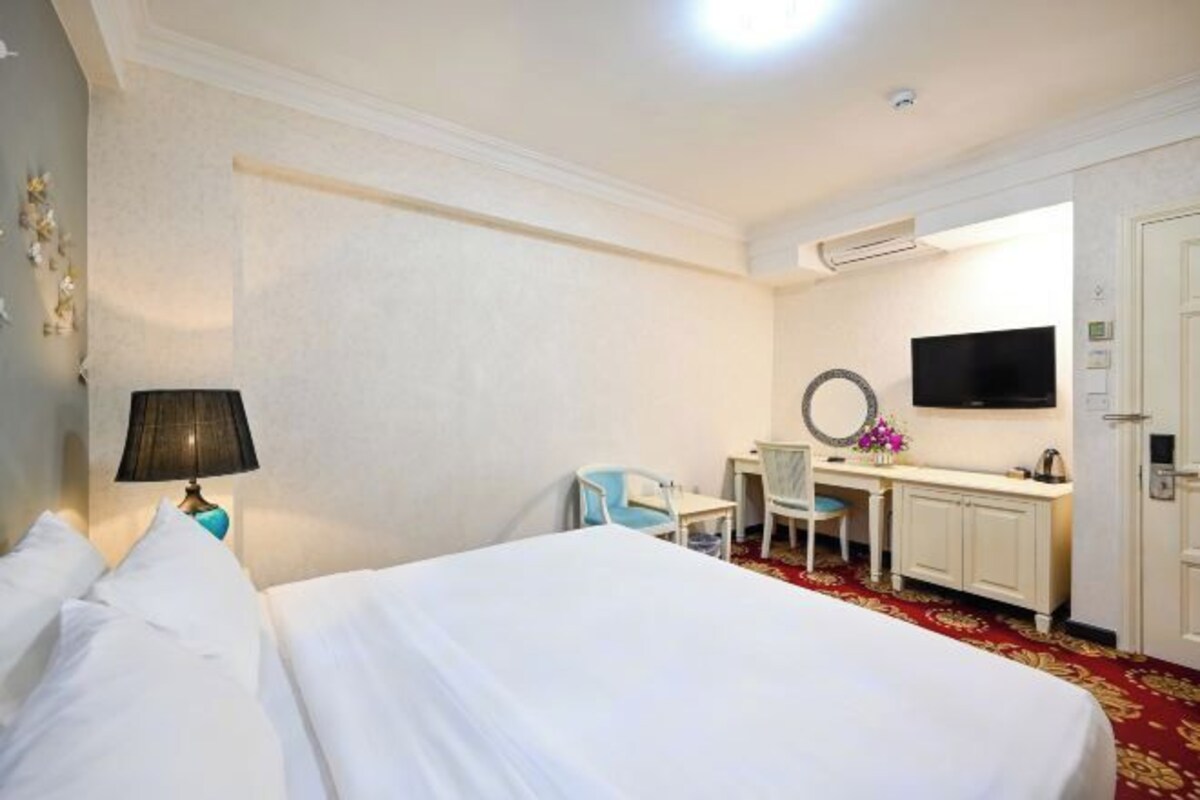 Habitación de hotel con una cama grande, un escritorio con silla, un televisor montado en la pared y una mesita con flores.