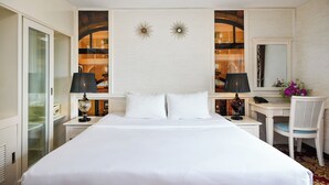 Una habitación de hotel con una cama grande, dos mesitas de noche, un escritorio, una silla, un espejo y apliques decorativos en la pared.