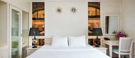 A hotel room with a large bed, two bedside tables, a desk, a chair, a mirror, and decorative wall sconces.