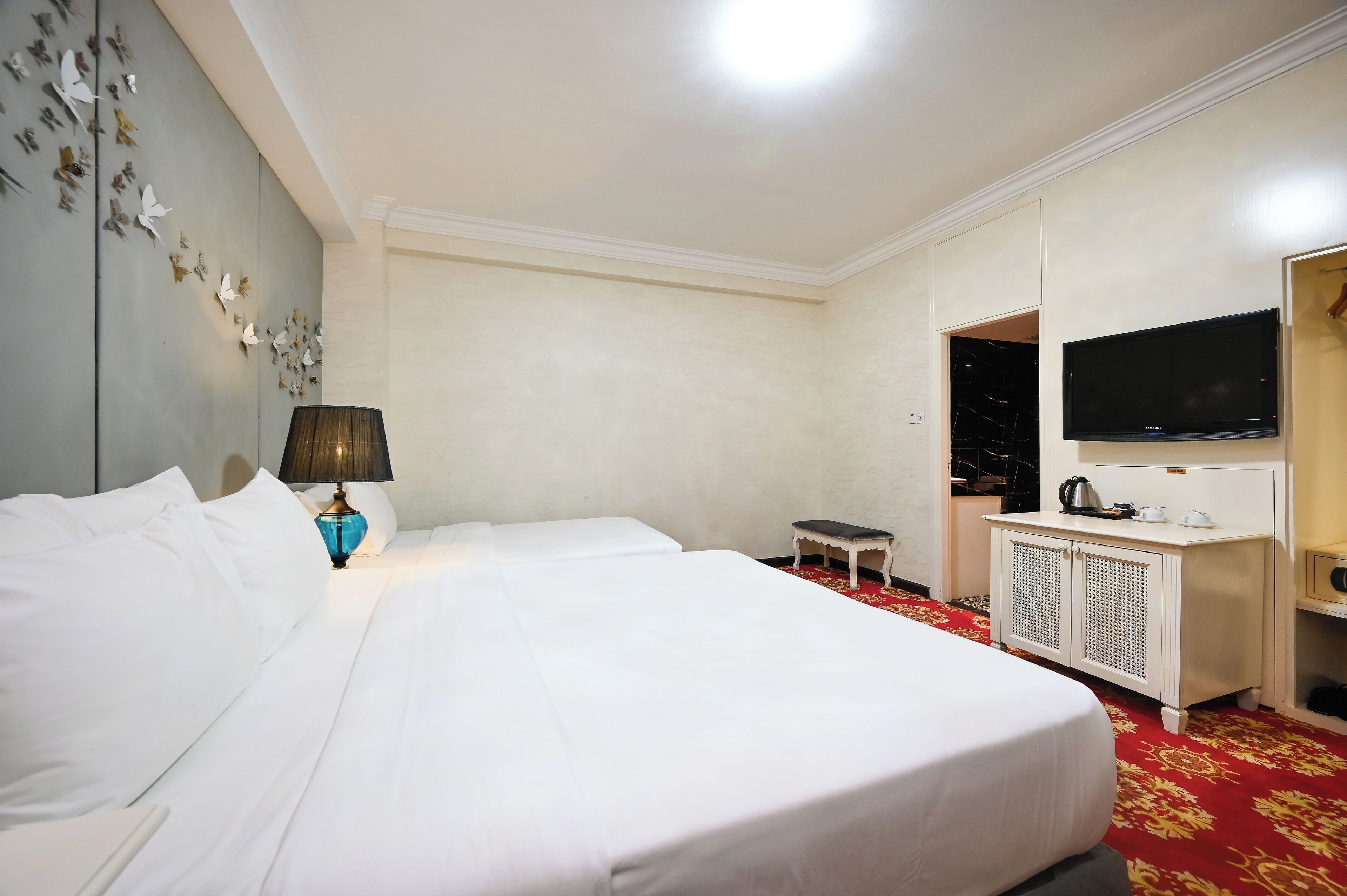 Hotellihuone, jossa on kaksi sänkyä, televisio, pieni pöytä ja kaappi.