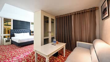 A hotel room with a bed, a wardrobe, a sofa, and a table with a water bottle.