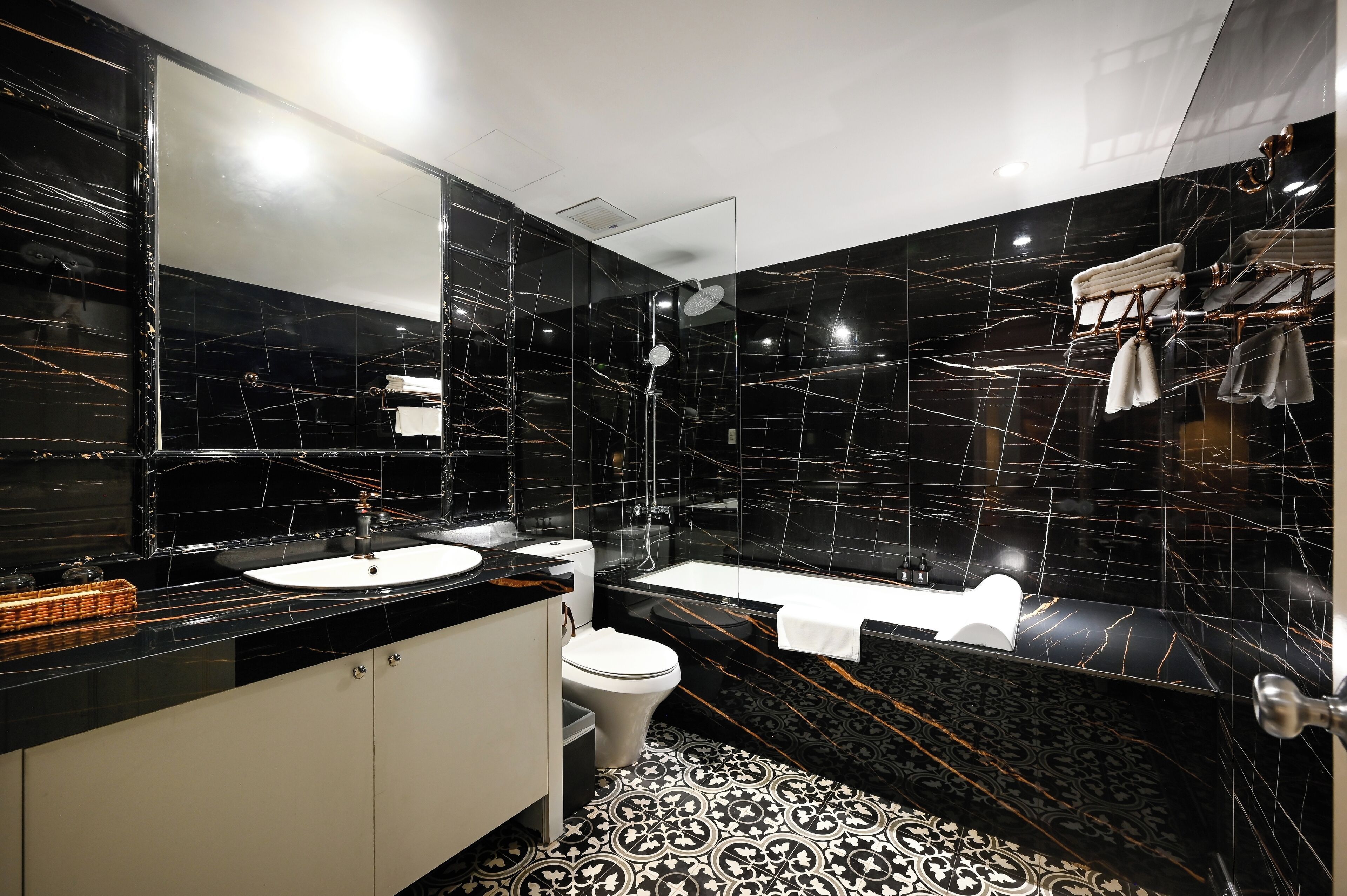 A modern bathroom with black marble walls, a white sink, a toilet, and a bathtub.