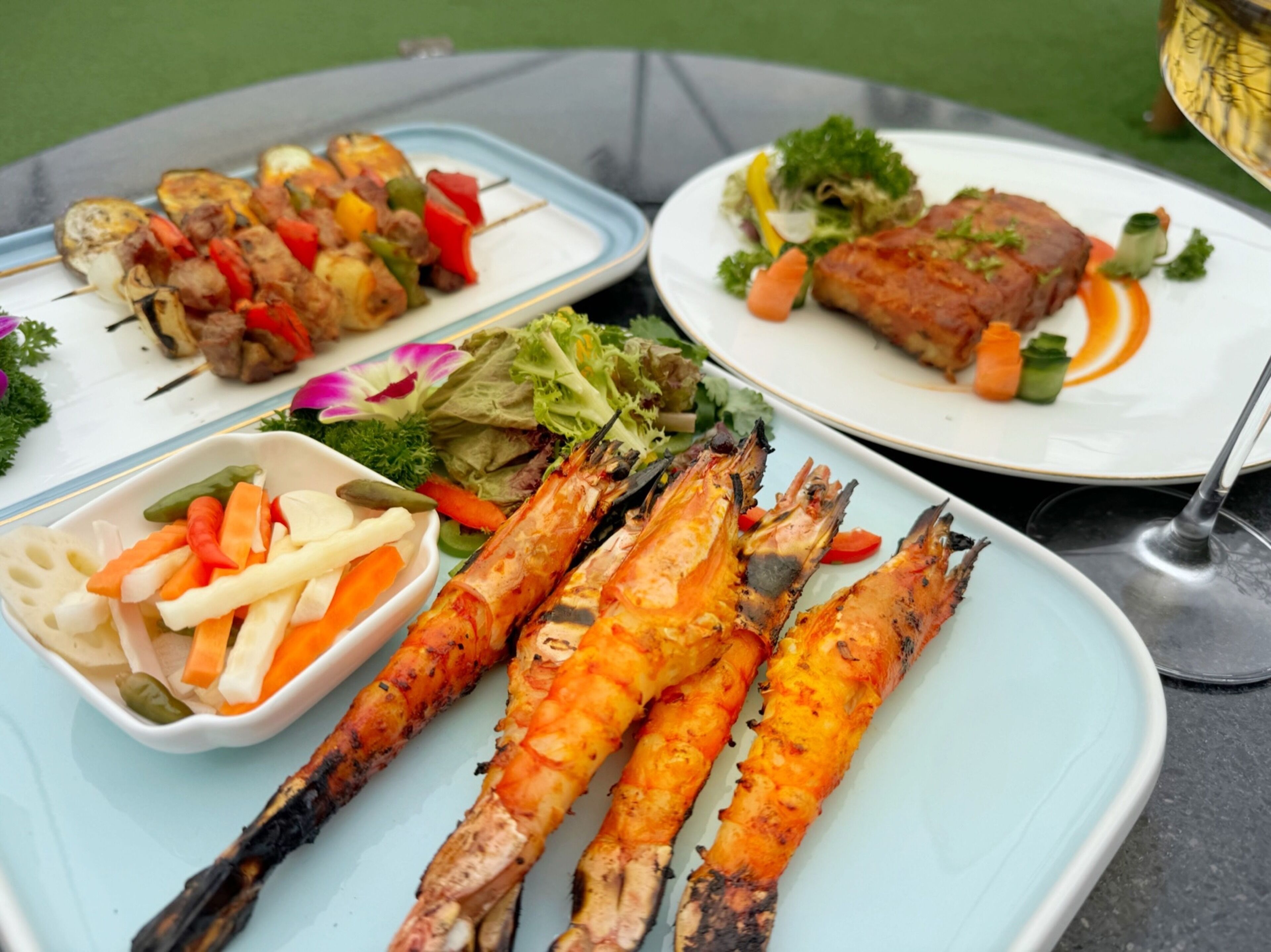 Een tafel met diverse gerechten, waaronder gegrilde garnalen, spiesjes en een salade.