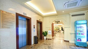 Un vestíbulo de hotel con piso de mármol, una máquina expendedora Sator! y un cartel sobre las normas del hotel.