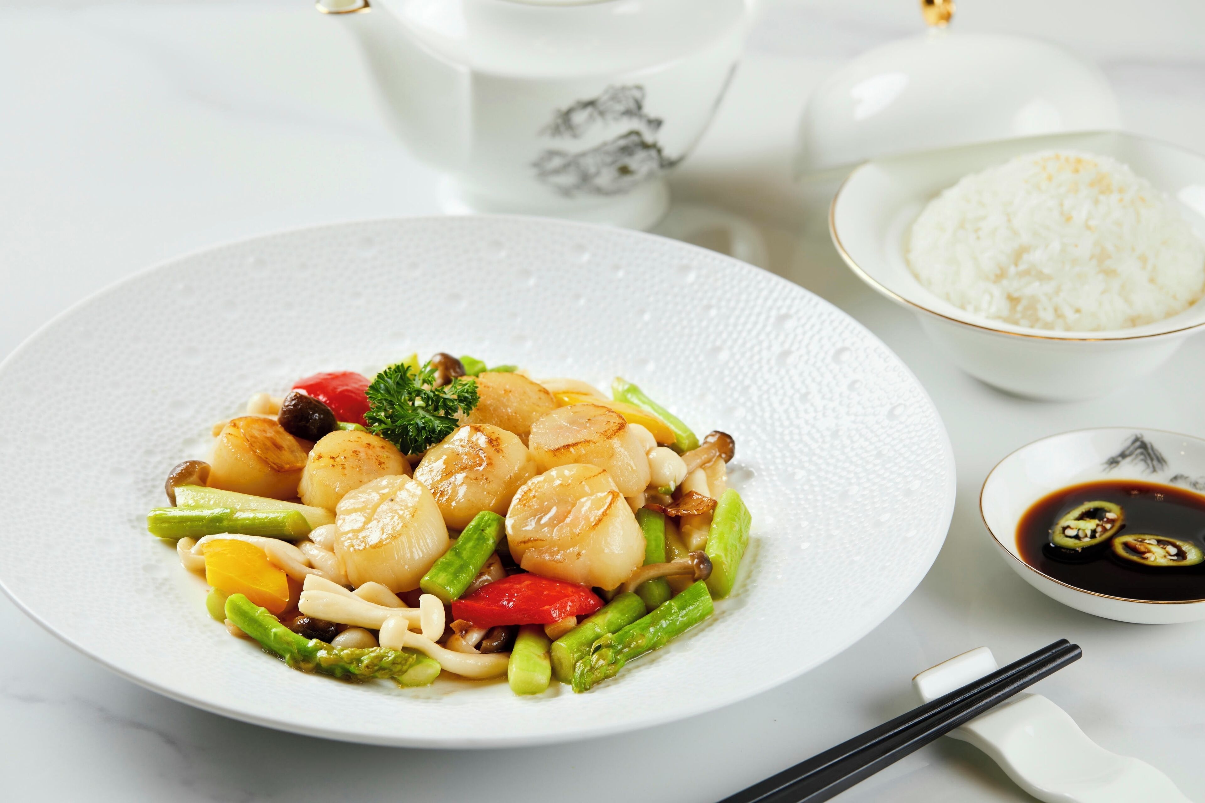 A plate of scallops with vegetables and a small bowl of soy sauce.