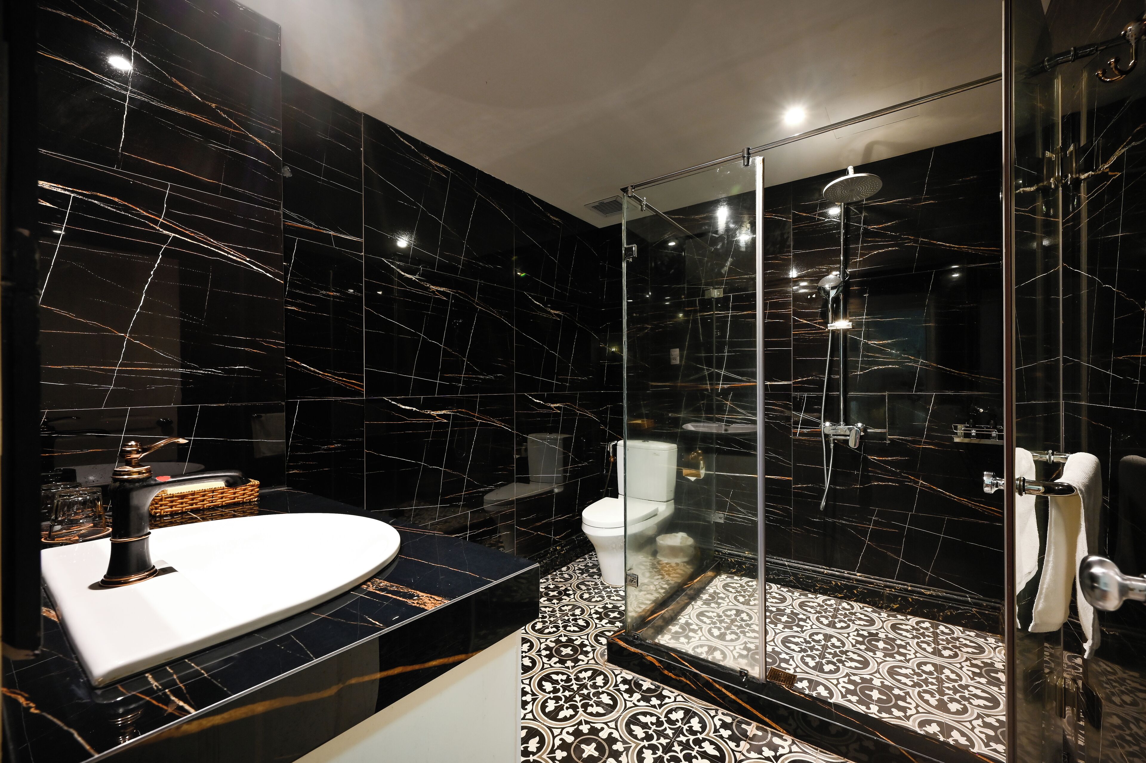 A modern bathroom with a black marble sink, a glass-enclosed shower, and patterned floor tiles.