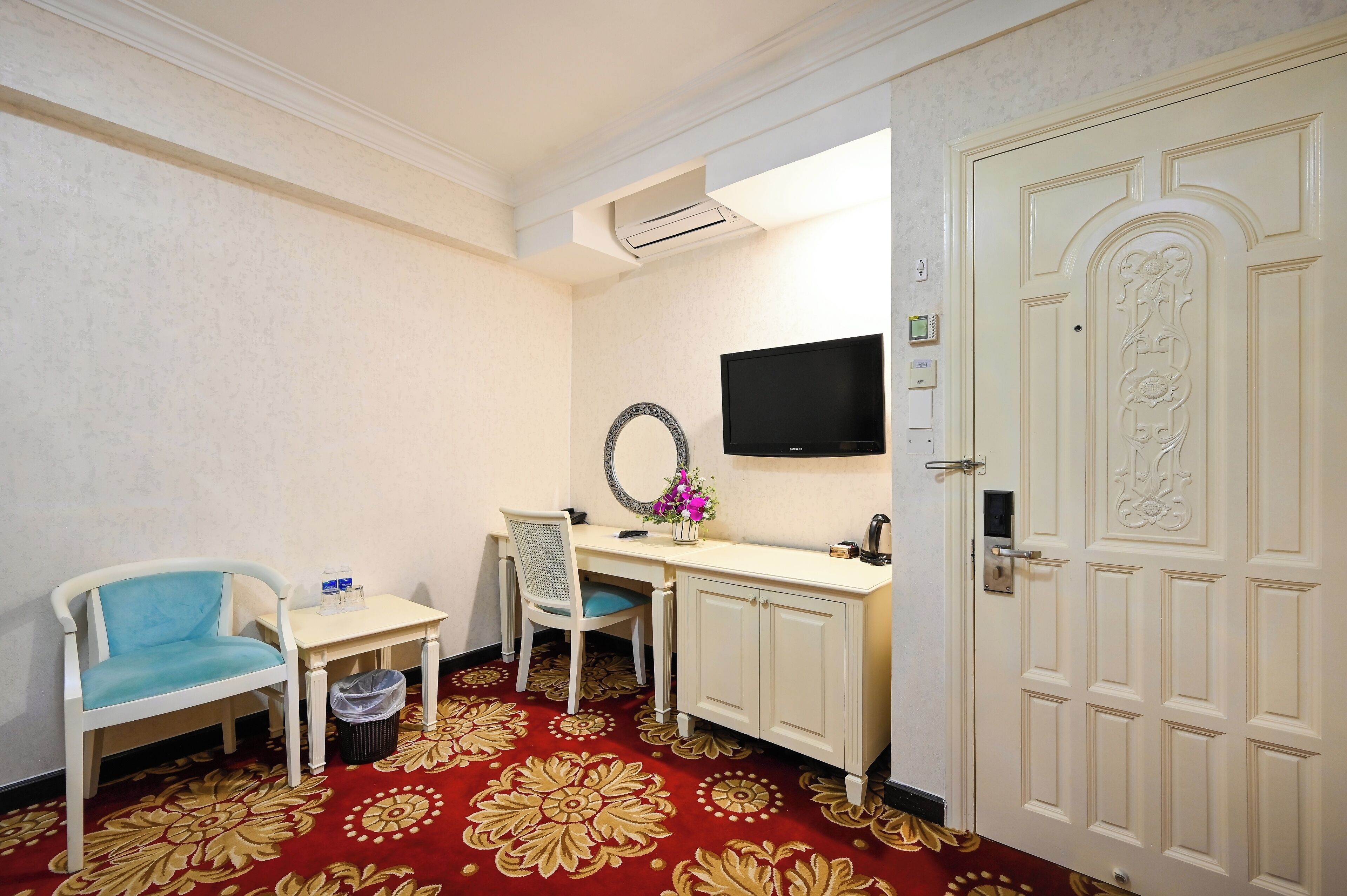 A hotel room with a desk, a chair, a TV, and a door.
