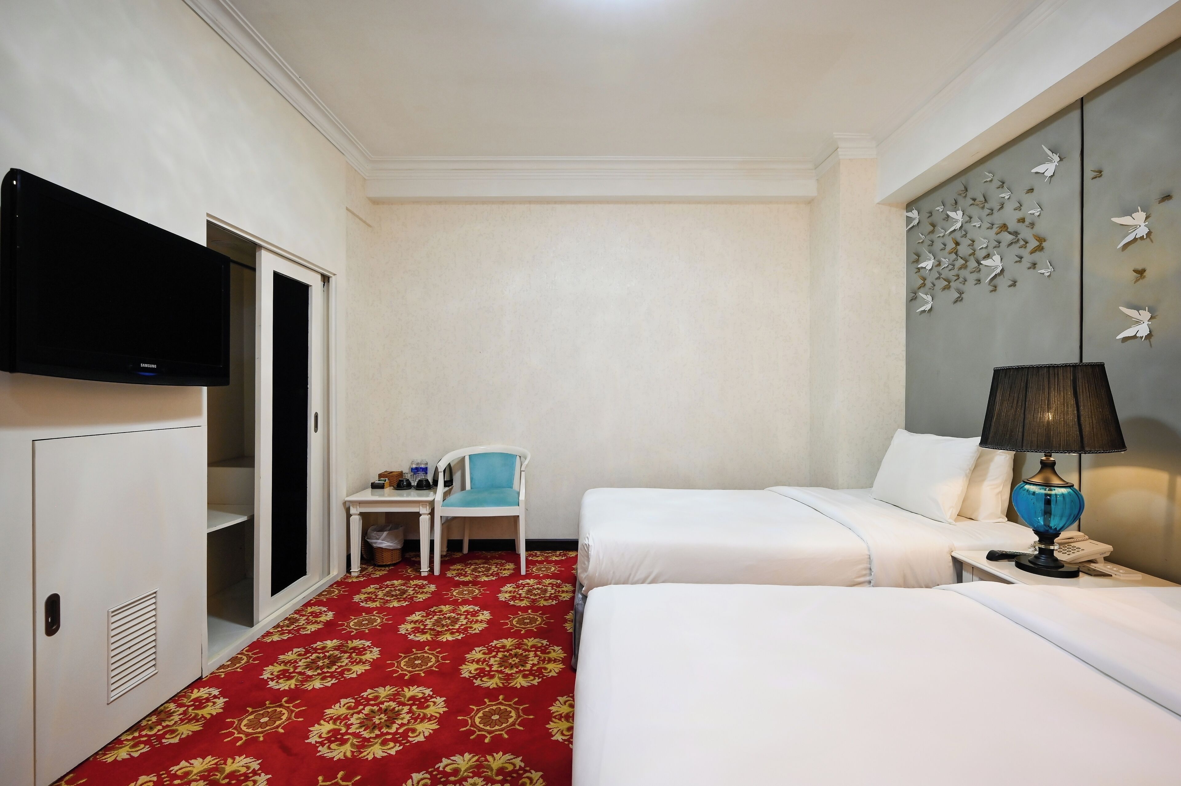 A hotel room with two beds, a desk, a chair, a television, and a decorative wall panel.